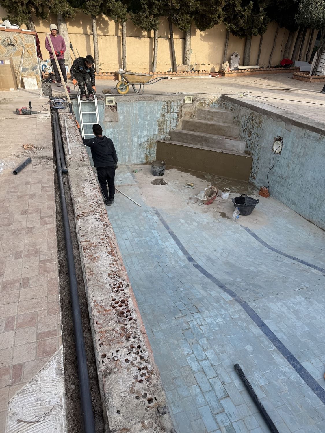 Personas trabajando en la renovación de una piscina vacía. Un entorno soleado al aire libre.