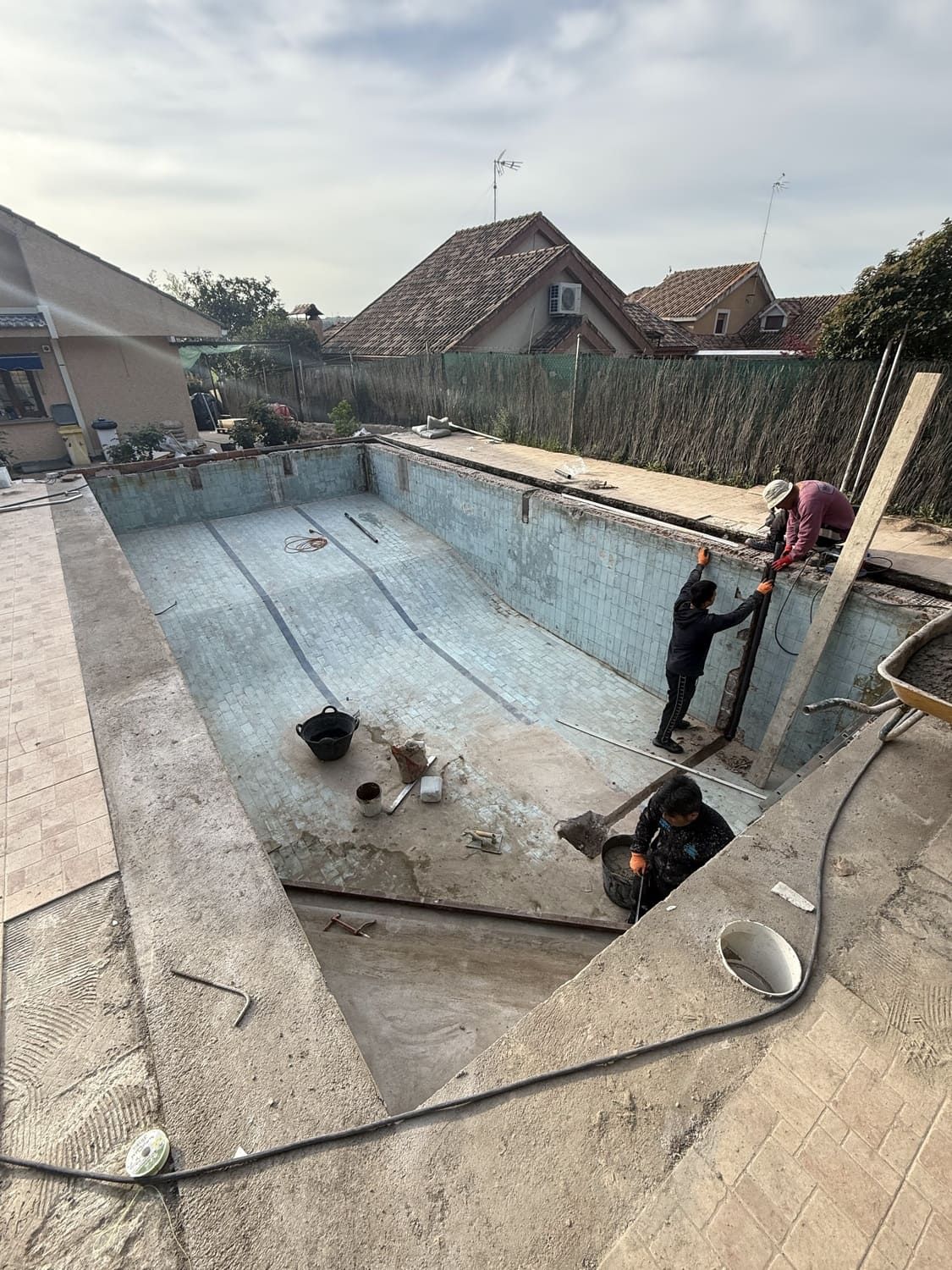 Obreros renovando una piscina vacía. Se ven equipos y materiales de construcción.