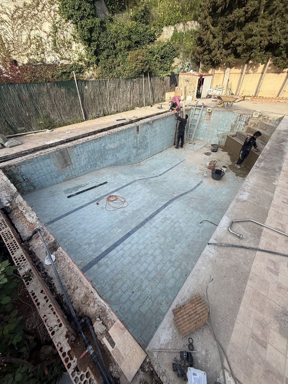 Obreros renovando una piscina rectangular vacía. El interior de la piscina tiene azulejos y marcas azules.