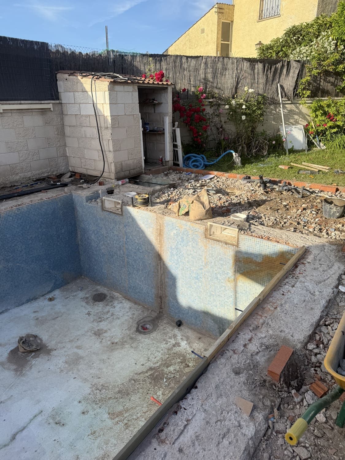 Piscina demolida con escombros, cobertizo adyacente y patio trasero residencial.