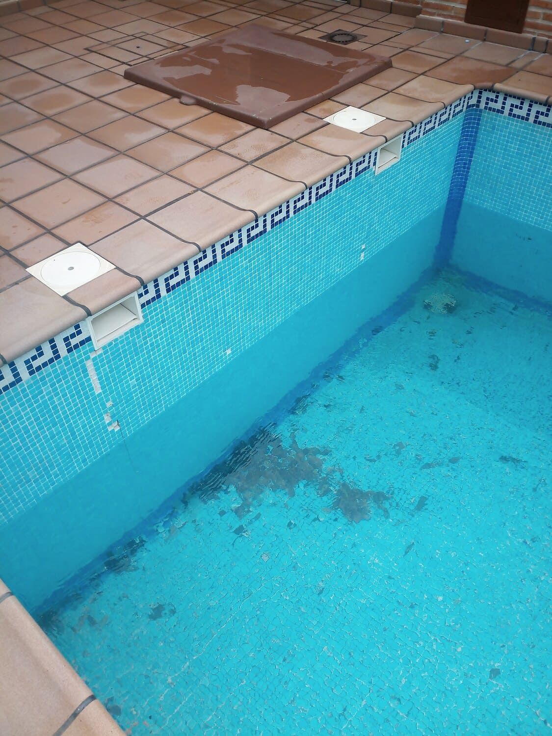 Una piscina parcialmente llena con azulejos azules, rodeada de azulejos color canela.