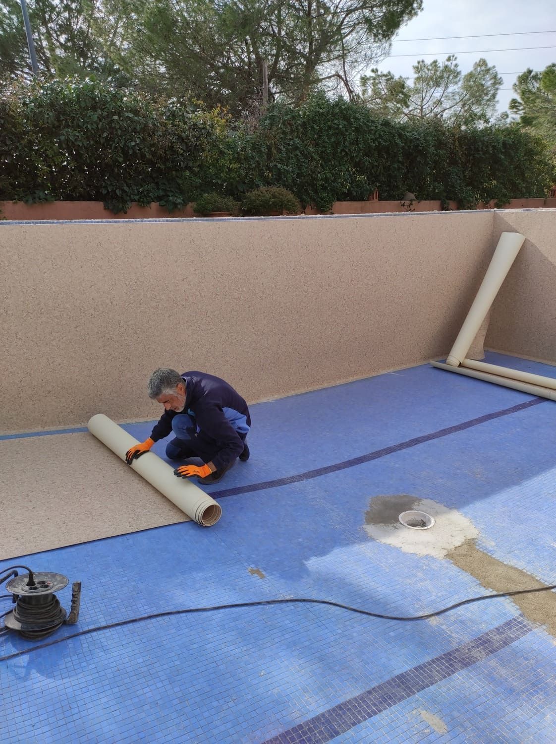 Una persona extiende material de color canela dentro de una piscina vacía con revestimiento azul.