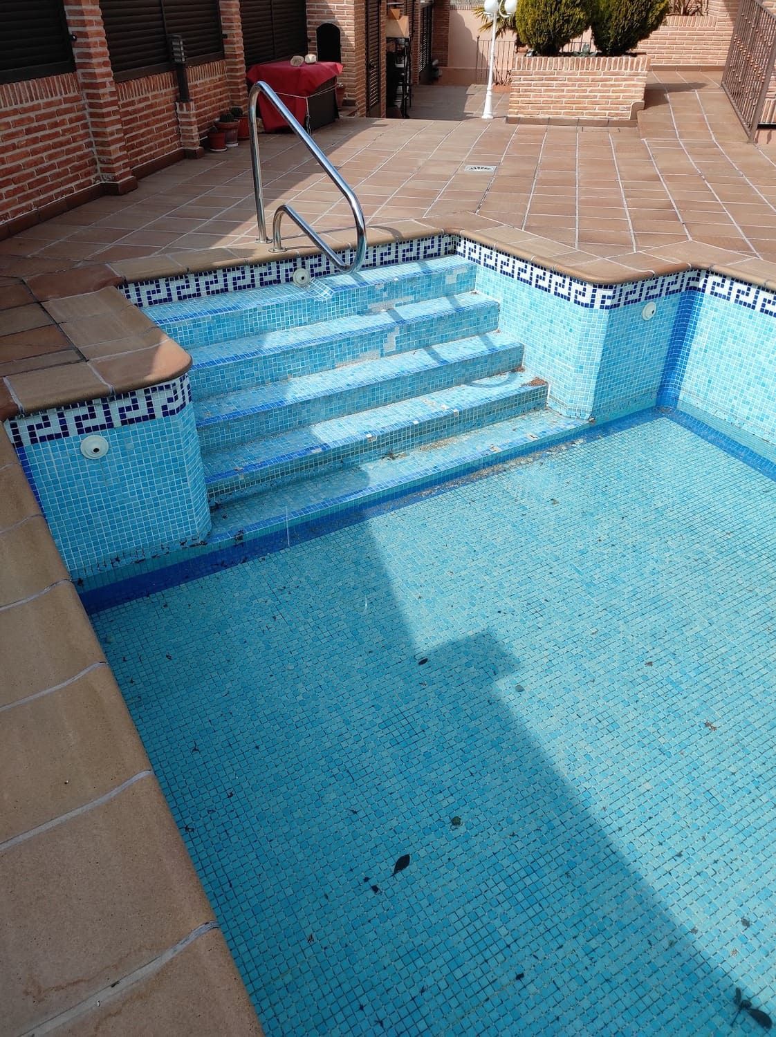 Piscina con azulejos azules y escalones, rodeada de patio de piedra.