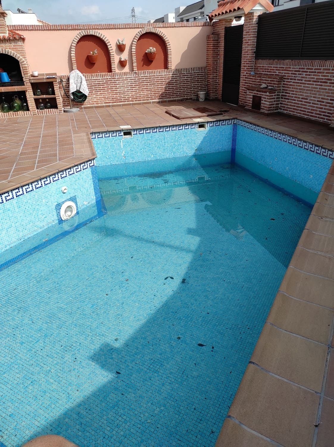 Piscina con azulejos azules en una terraza en la azotea, rodeada de paredes de ladrillo y terracota.