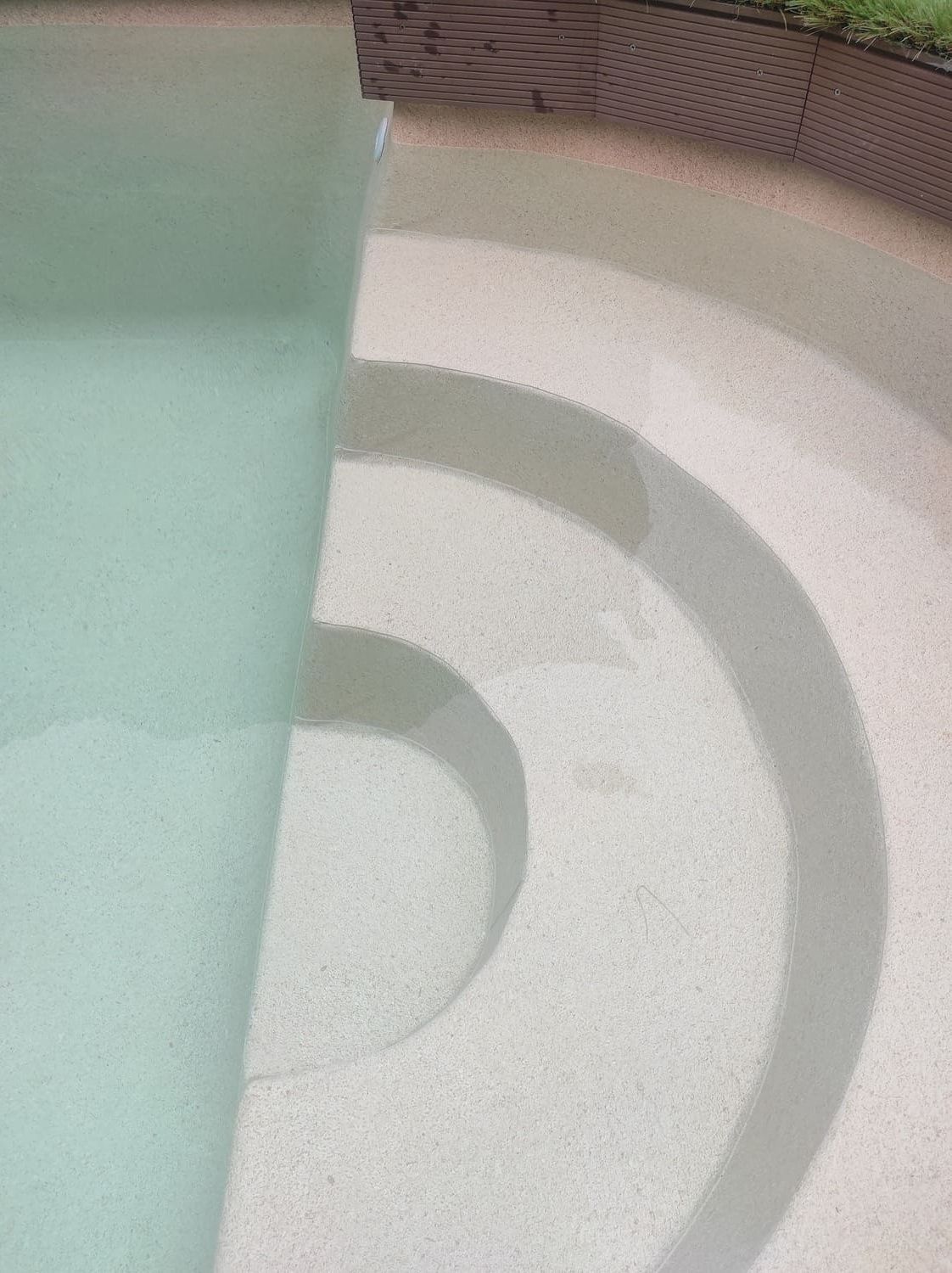 Escaleras de piscina con agua clara y hormigón texturizado de color claro.