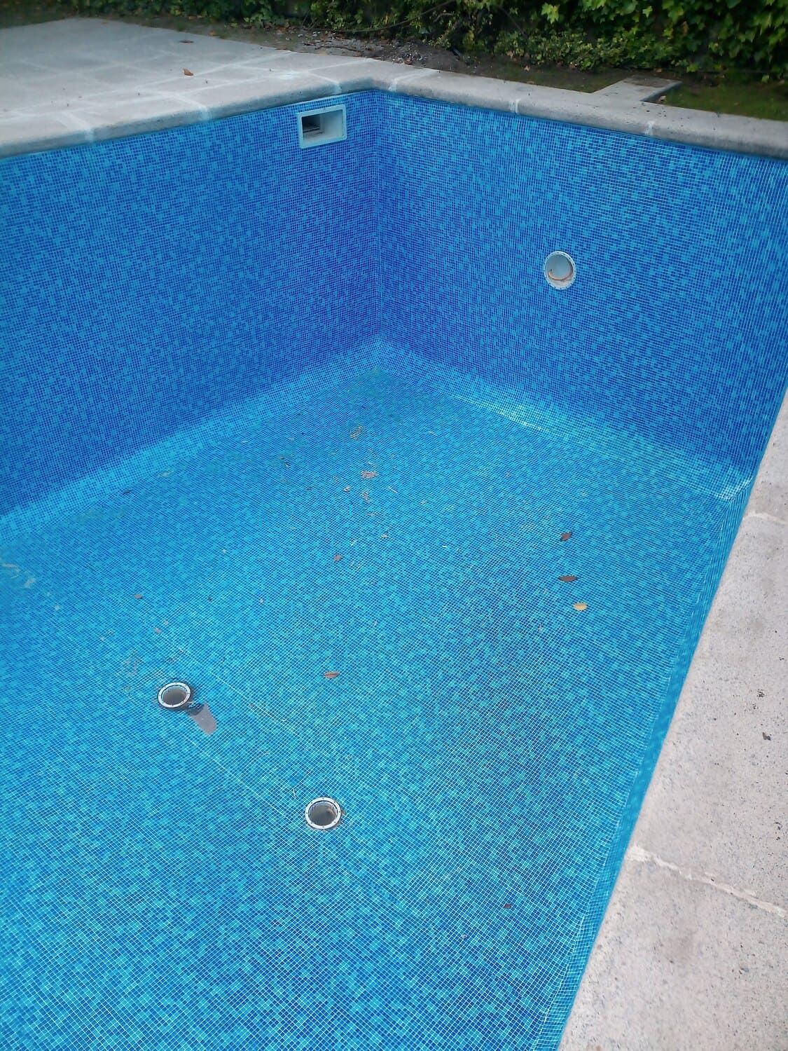 Piscina vacía de azulejos azules, con borde de piedra blanca.