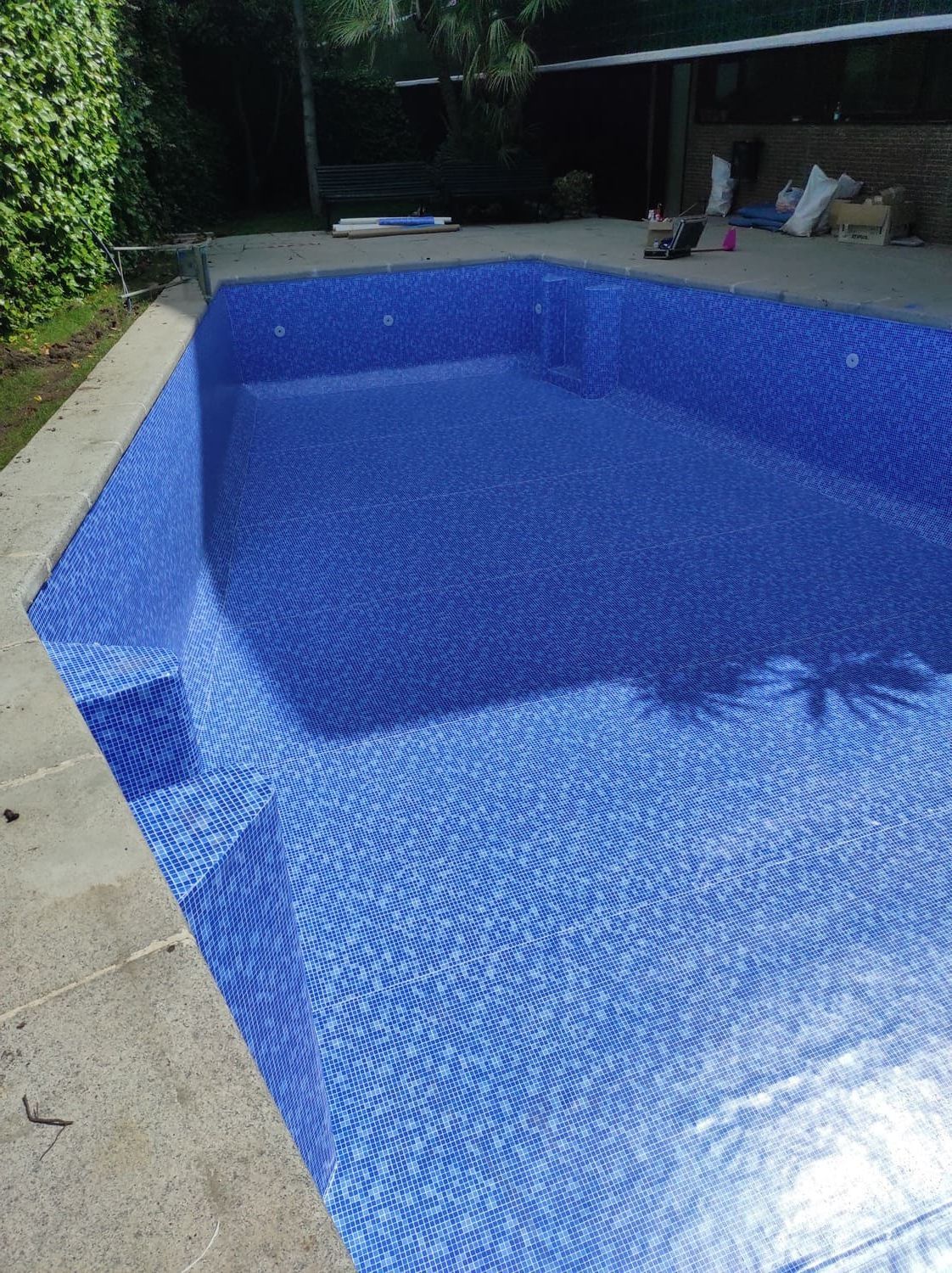 Piscina vacía revestida con pequeños azulejos azules y rodeada por un borde de hormigón.