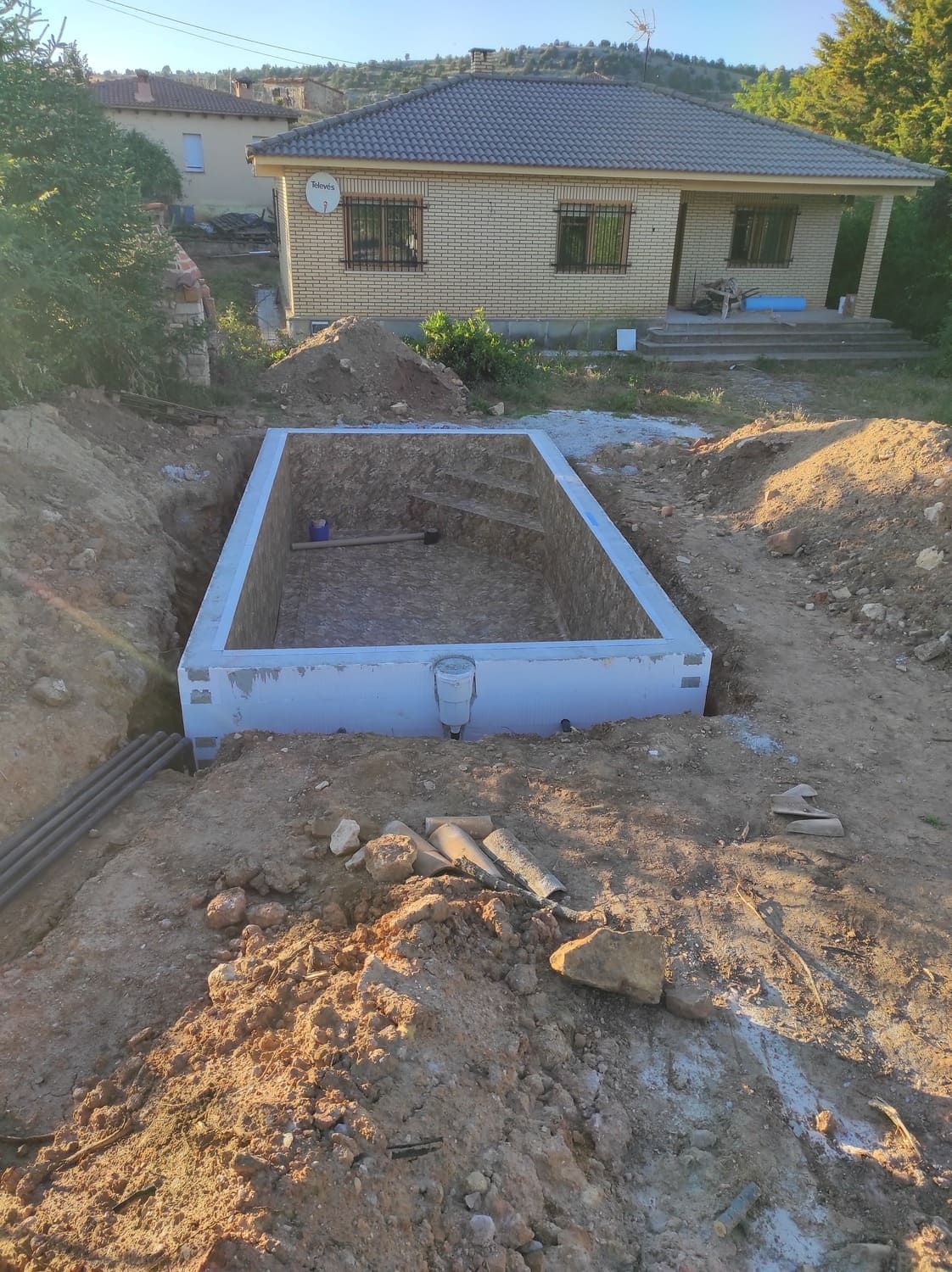 Una estructura rectangular de hormigón gris en una excavación de tierra; una casa al fondo.