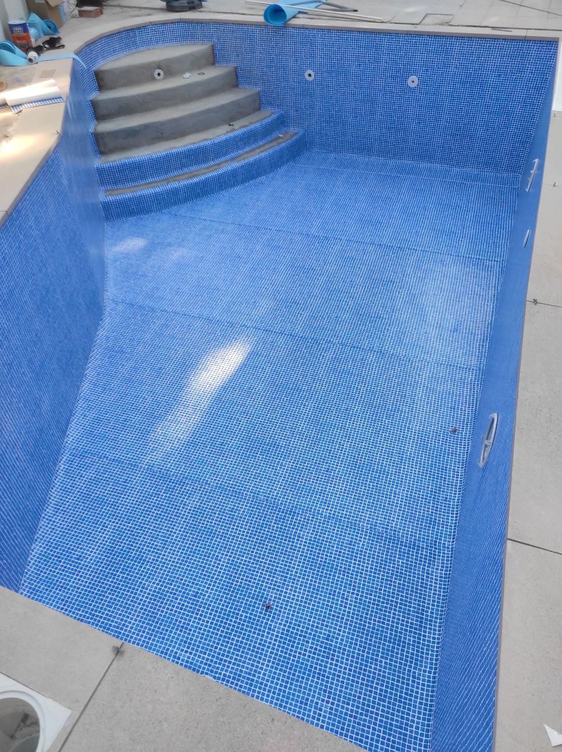 Piscina de azulejos azules en construcción, con escalones e iluminación.