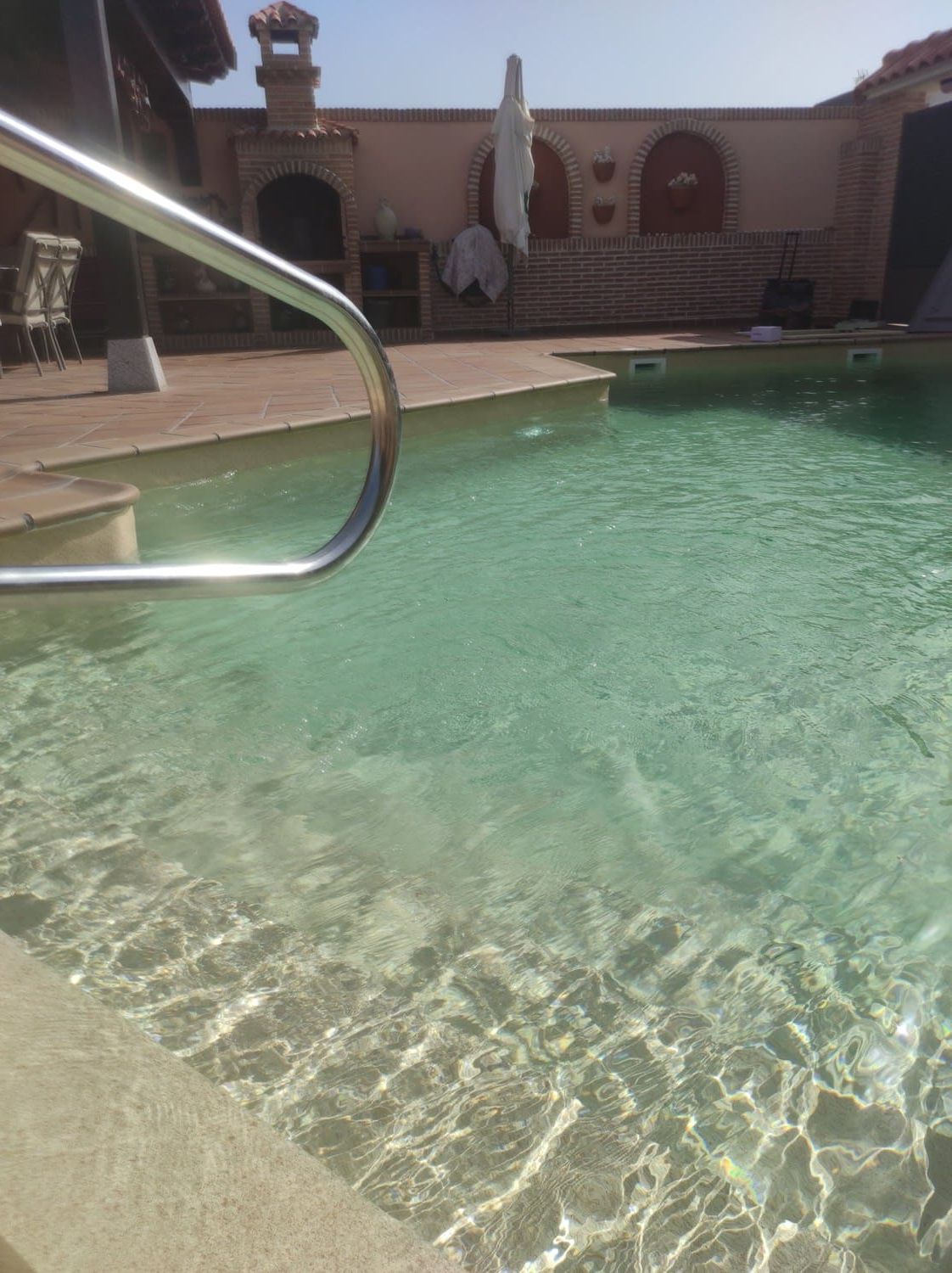 Piscina con agua cristalina y barandilla metálica, entorno exterior soleado.
