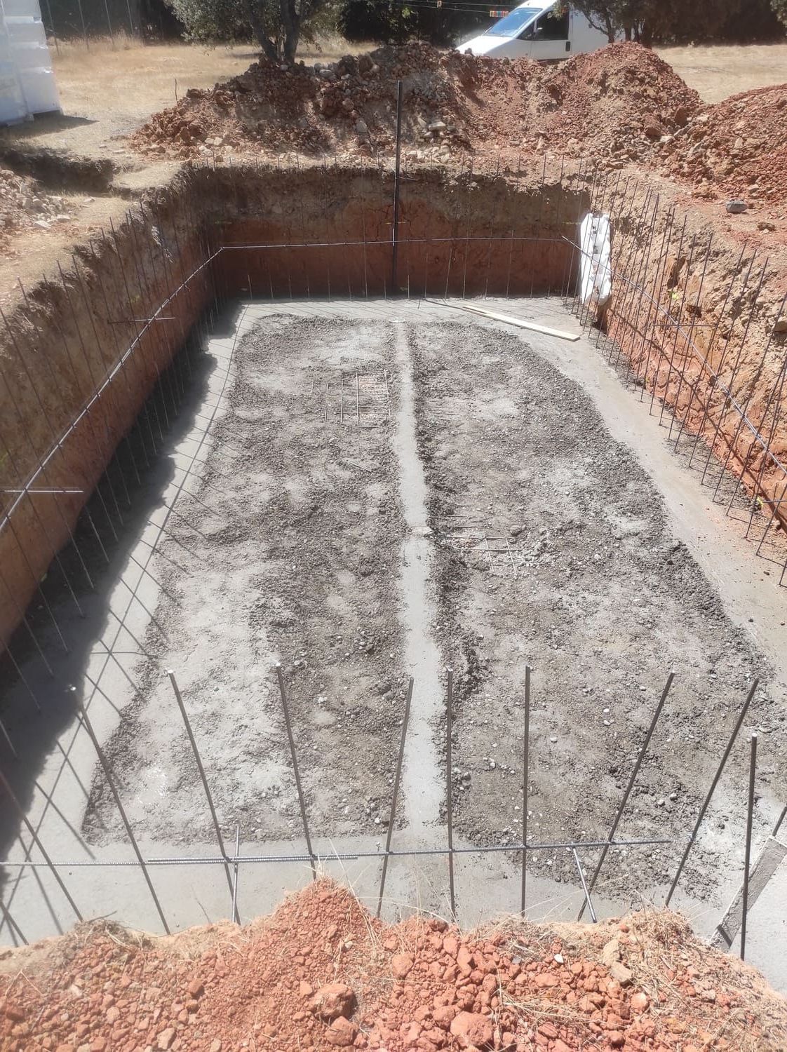 Sitio de construcción con un agujero rectangular excavado en el suelo, que muestra el trabajo de hormigón con barras de refuerzo.