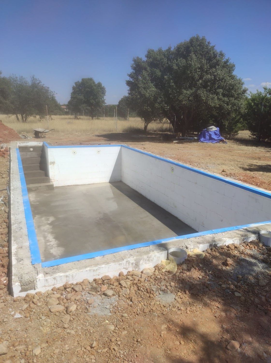 Piscina rectangular vacía en construcción al aire libre, con moldura azul y escalera.