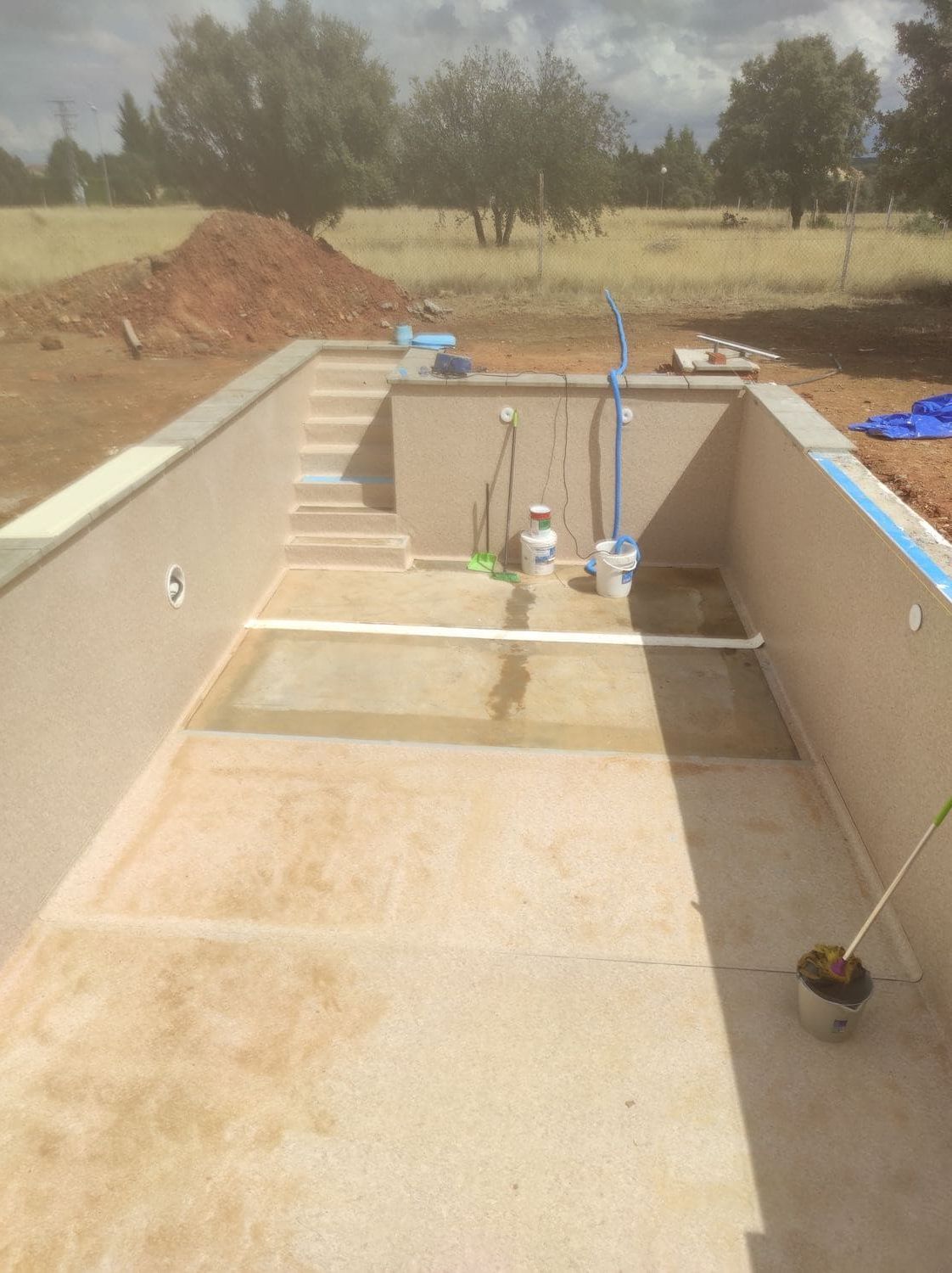 Piscina vacía en construcción con escalones, tuberías y paredes de hormigón.