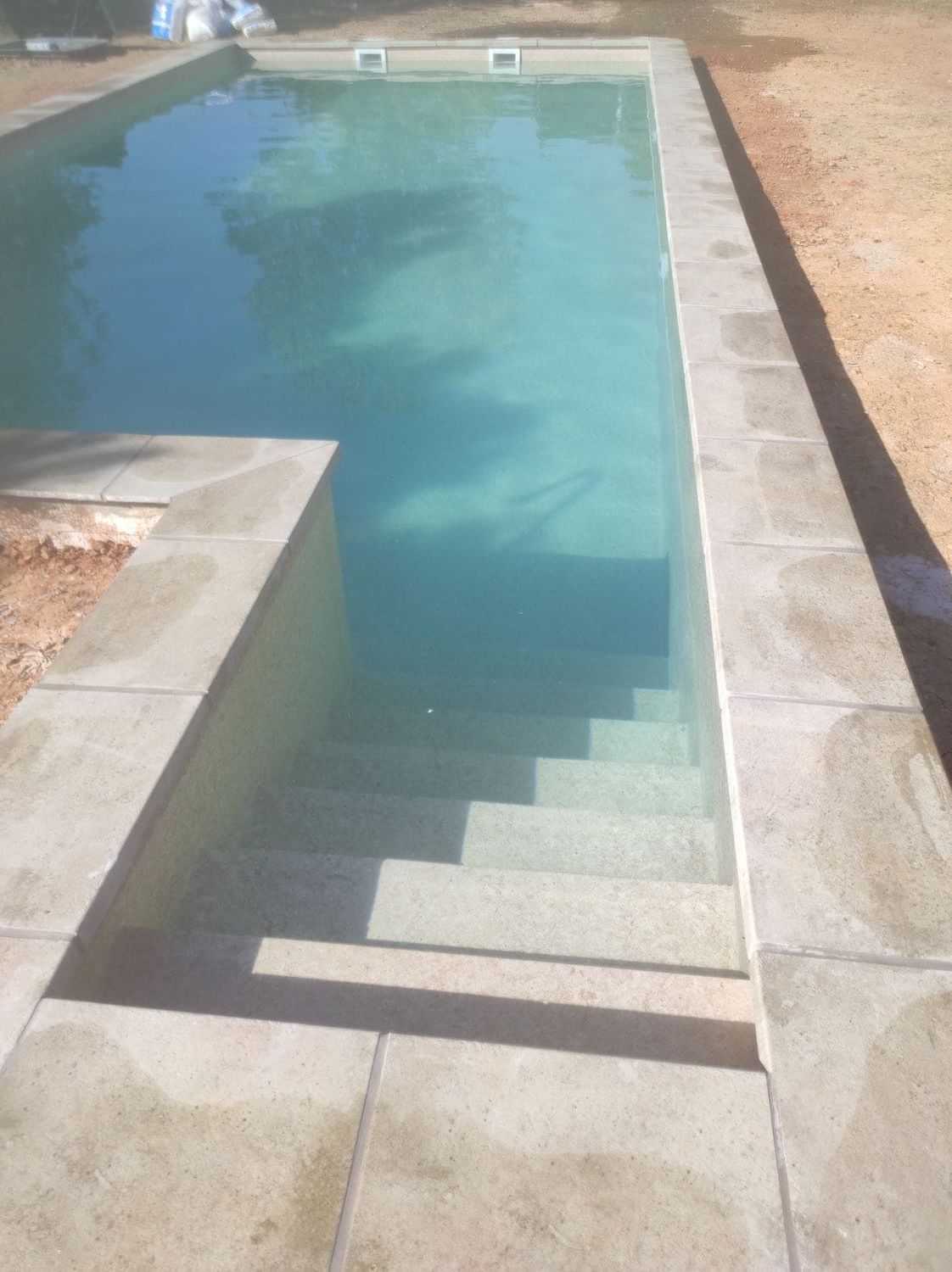 Una piscina rectangular con escalones incorporados y agua de color azul claro, rodeada de hormigón.