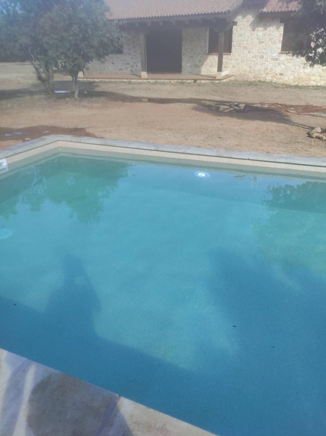 Piscina que refleja una luz, con una casa de piedra al fondo.