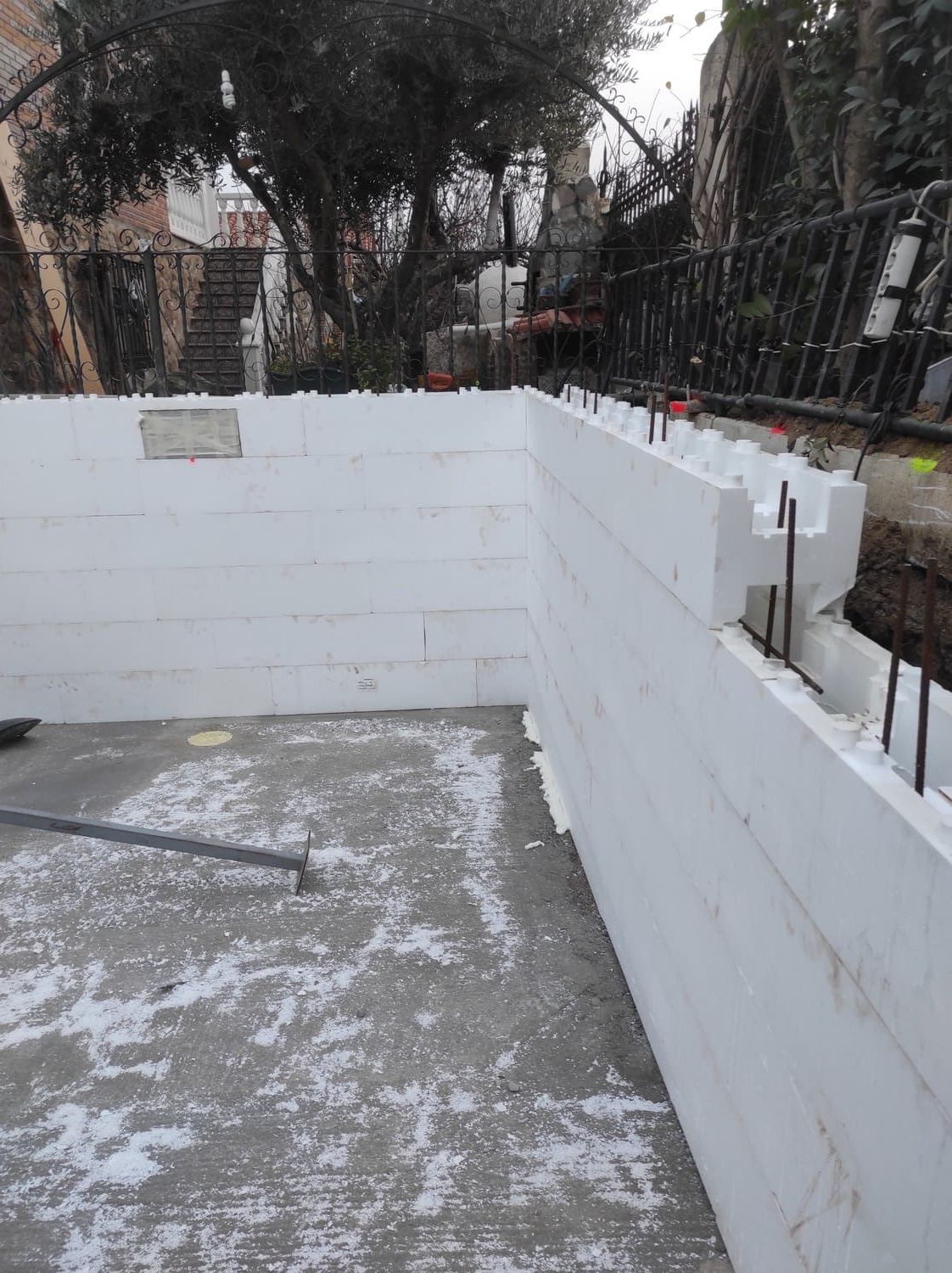 Obra: muros de bloques de espuma blanca en construcción. Varillas de refuerzo visibles. Suelo de hormigón.