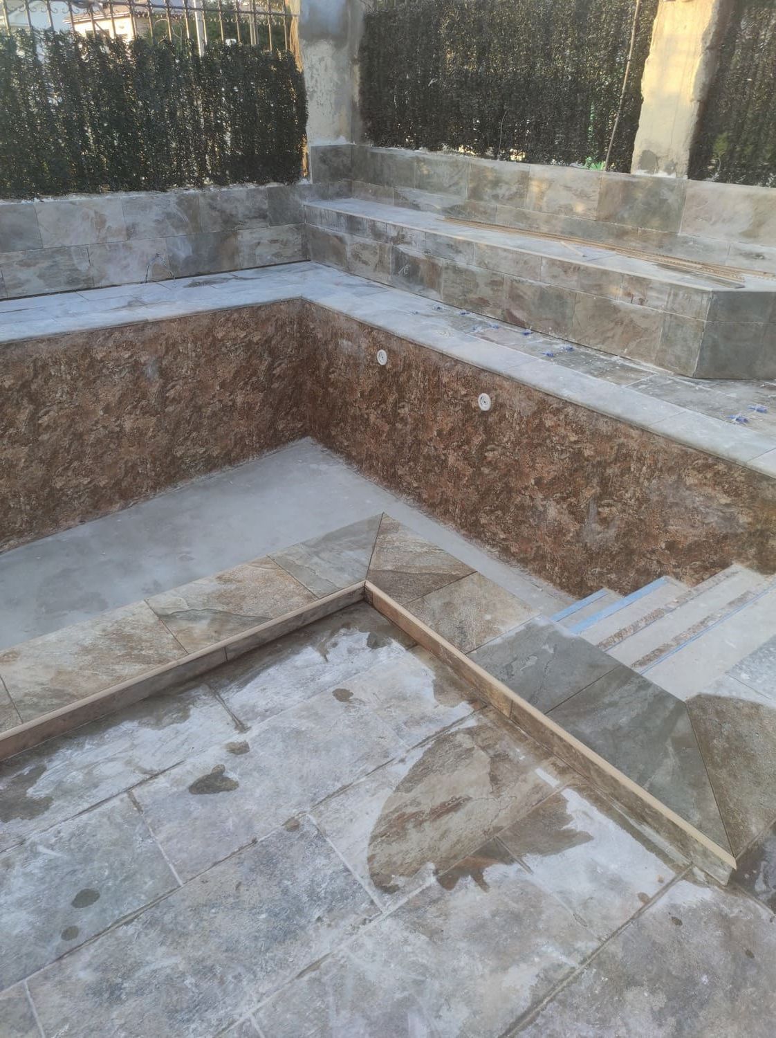 Piscina de piedra vacía con interior de azulejos, escalones y patio circundante.