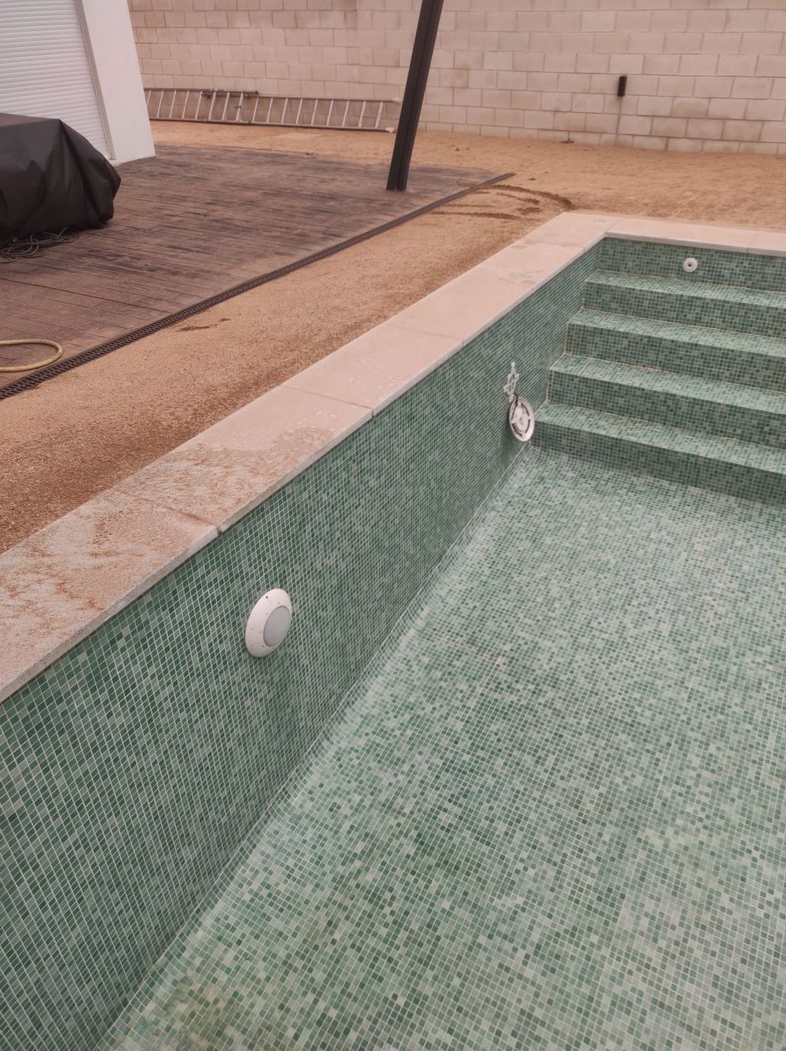 Piscina de mosaico verde con escalones, luces y borde de piedra.