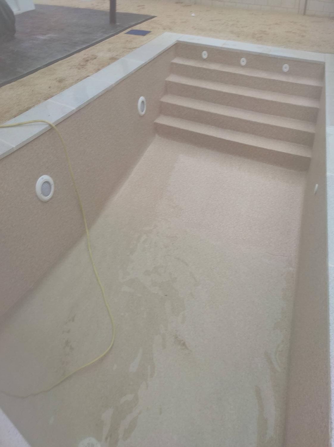 Piscina vacía de color beige con escalones y cuatro luces subacuáticas.