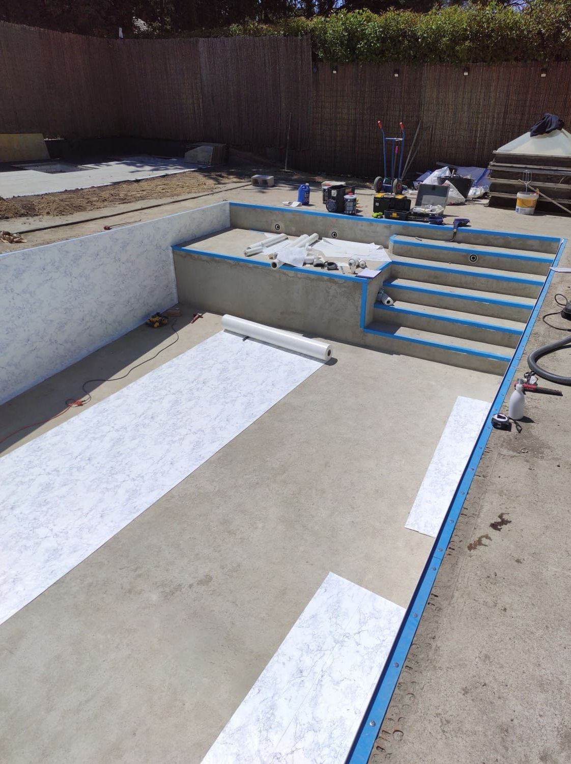 Construcción de la piscina: estructura de hormigón con escalones y revestimiento de papel. Borde azul visible.