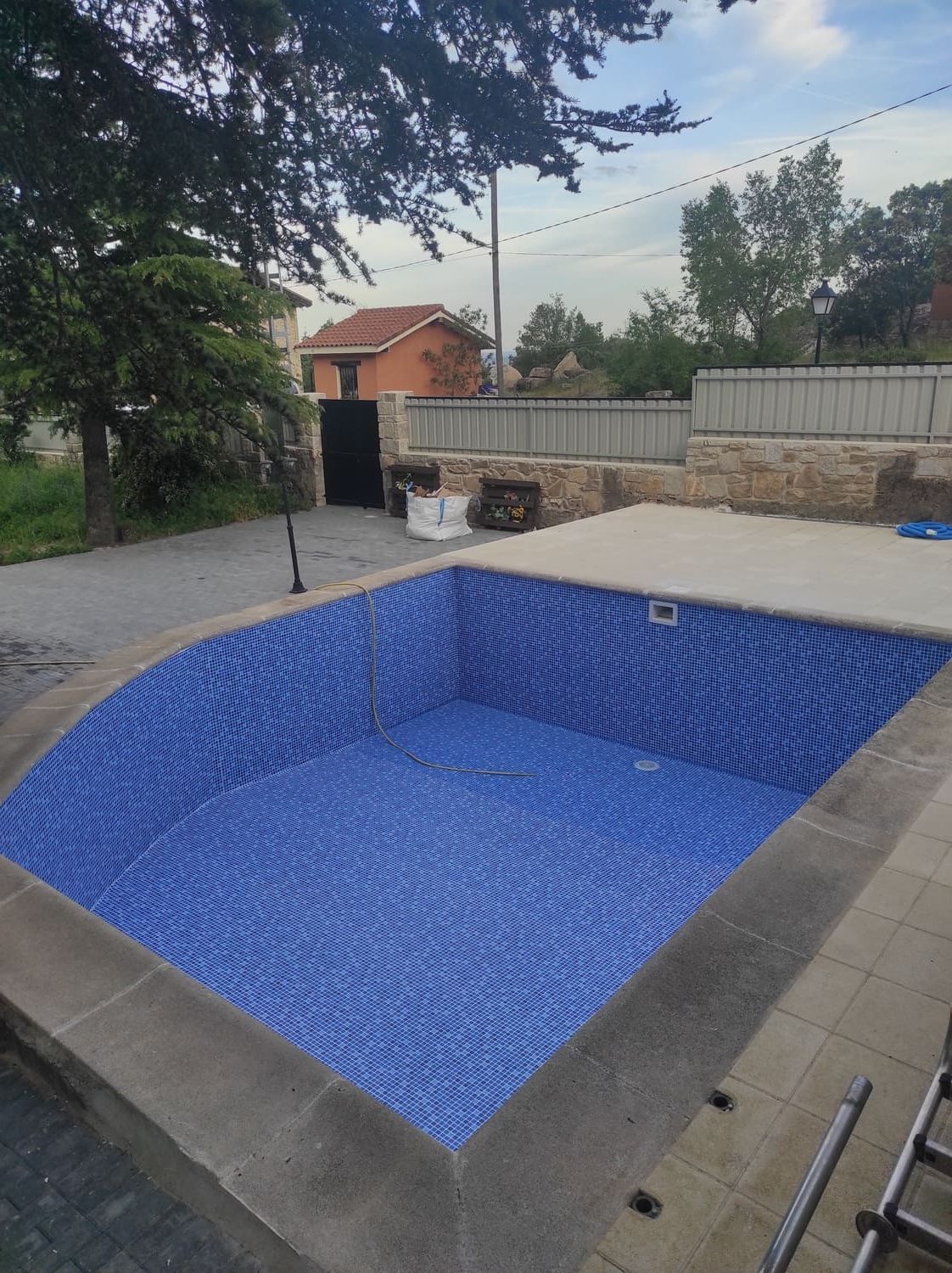 Piscina vacía con interior de azulejos azules. Borde de hormigón gris. En un patio trasero.