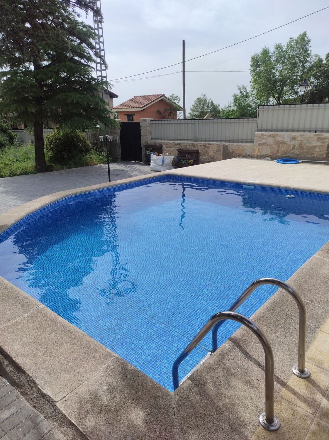 Piscina con interior de azulejos azules, escalera de metal, marco de hormigón y patio.