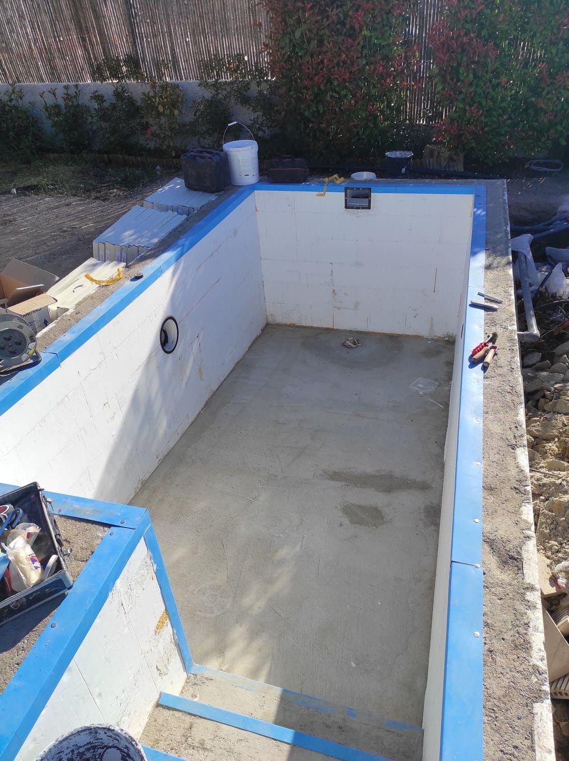 Piscina vacía en construcción, paredes blancas con detalles azules y suelo de hormigón. Exterior.