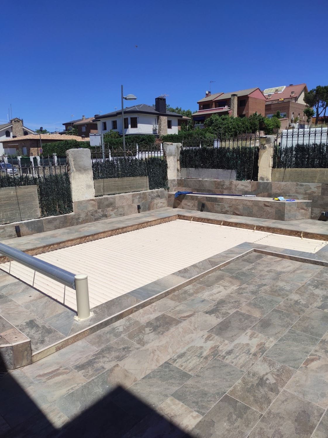 Patio de baldosas con superficie rectangular parcialmente cubierta, rodeado de muros bajos y verja de hierro forjado.