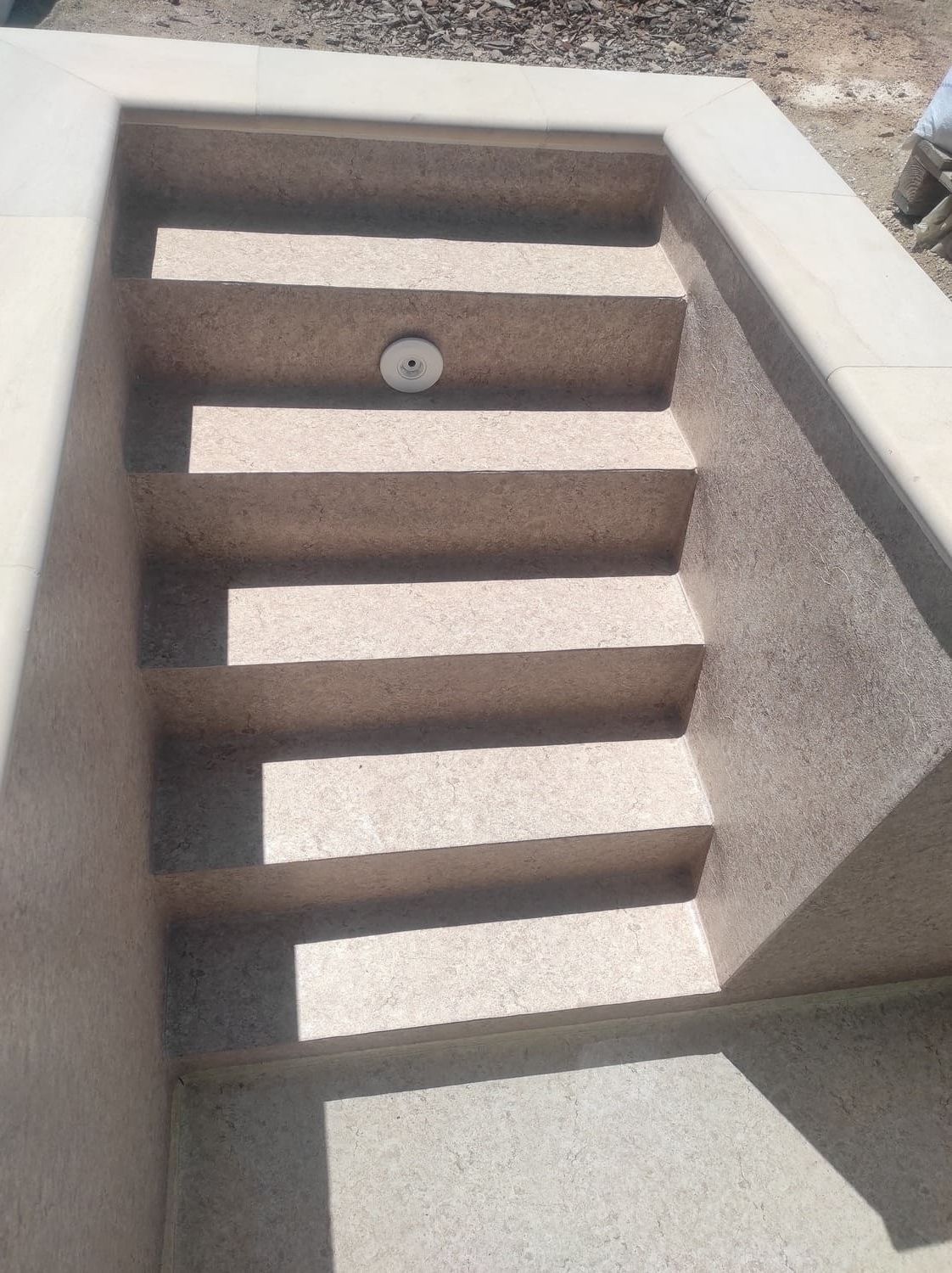 Escalones de piedra beige claro que descienden a un espacio empotrado. Lámpara redonda en el tercer escalón.