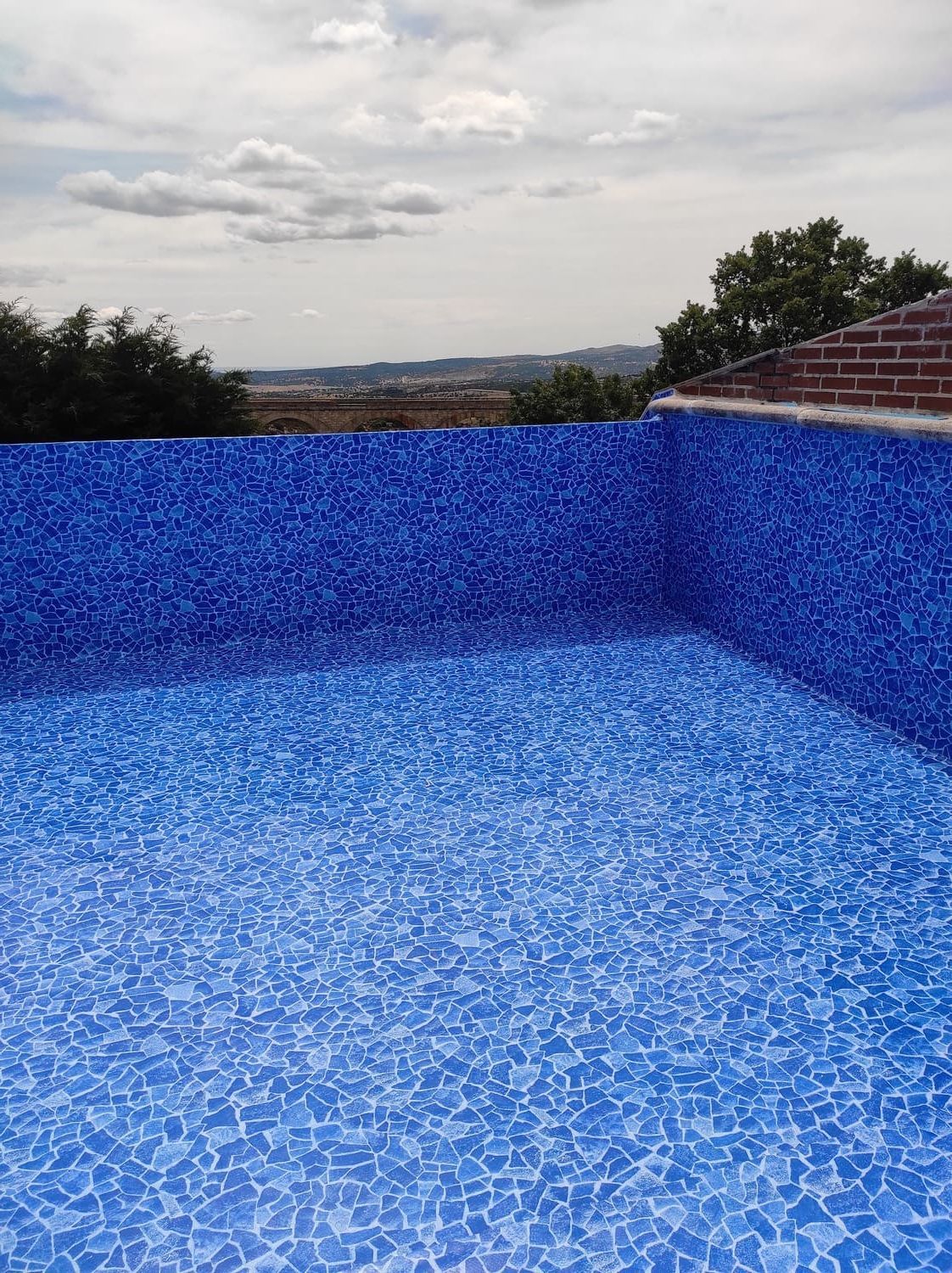 Piscina vacía de azulejos azules con vista al paisaje urbano distante y al cielo nublado.