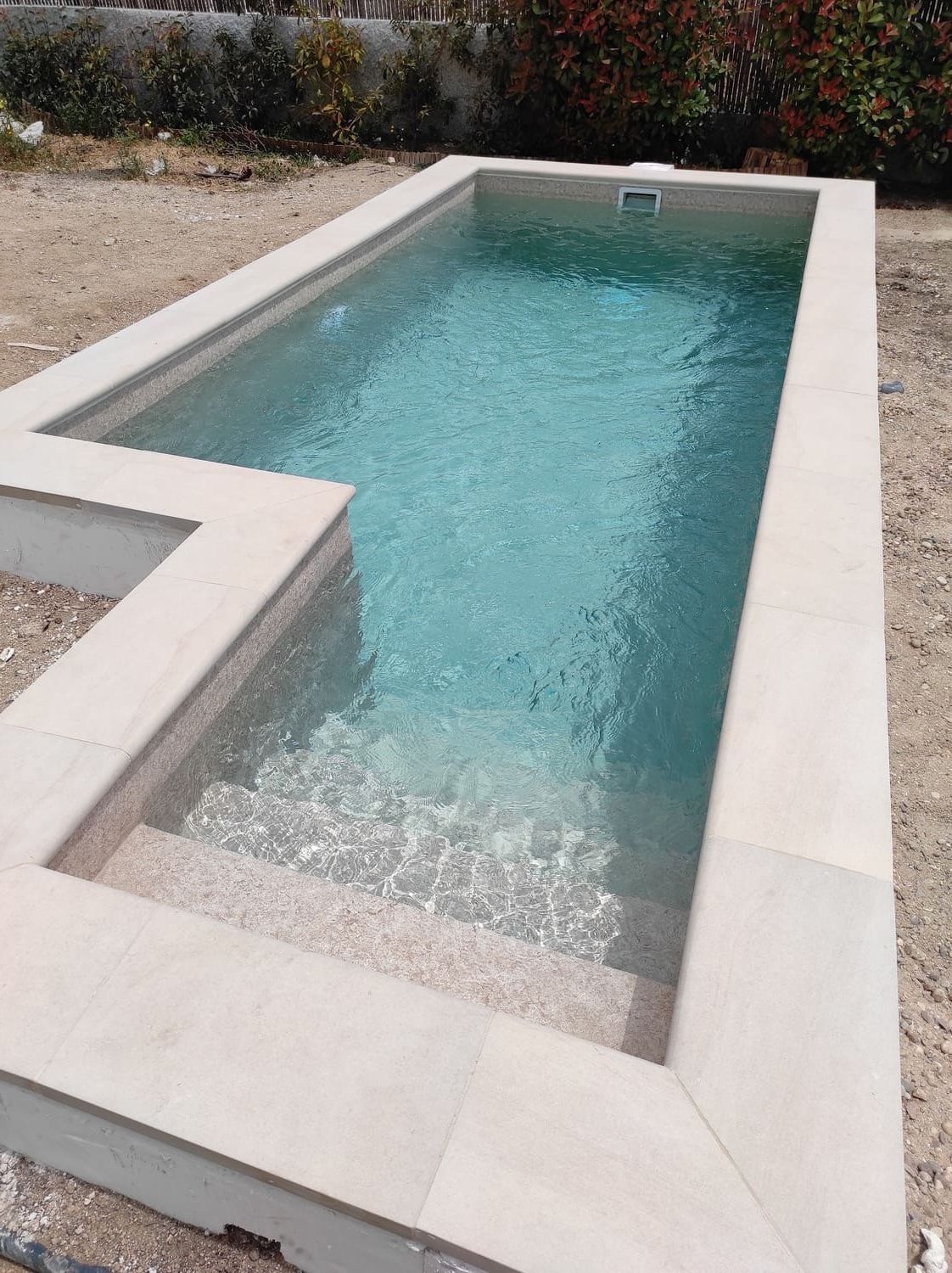 Piscina rectangular con borde de azulejos claros y escalones empotrados. El agua es de color turquesa claro.