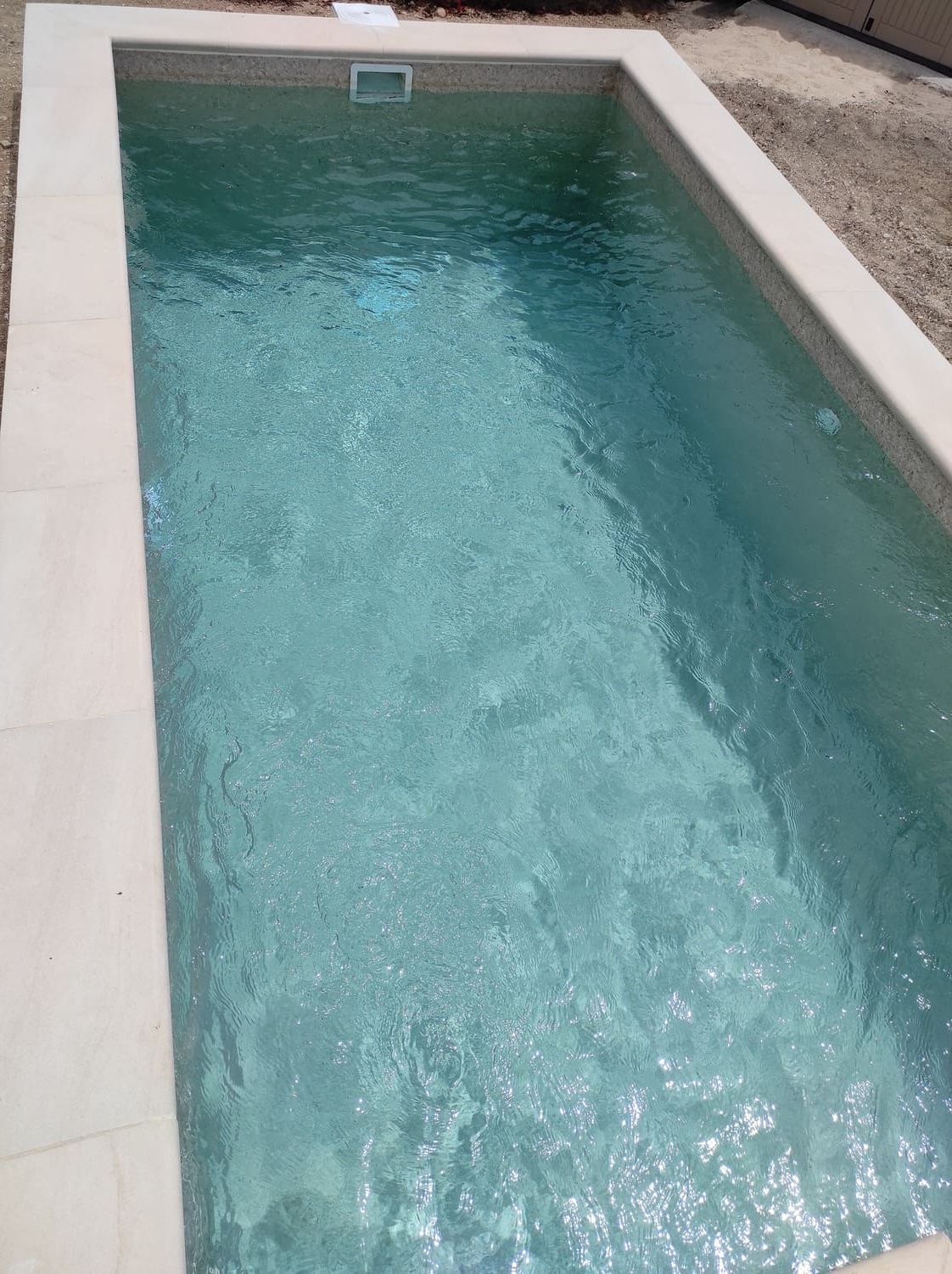 Piscina rectangular de agua clara y turquesa, rodeada de piedra beige.