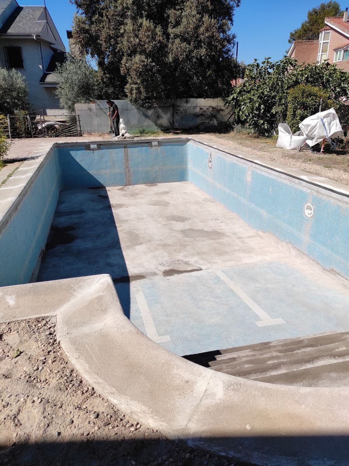 Piscina vacía, rectangular, con azulejos azules, en un entorno de patio trasero.