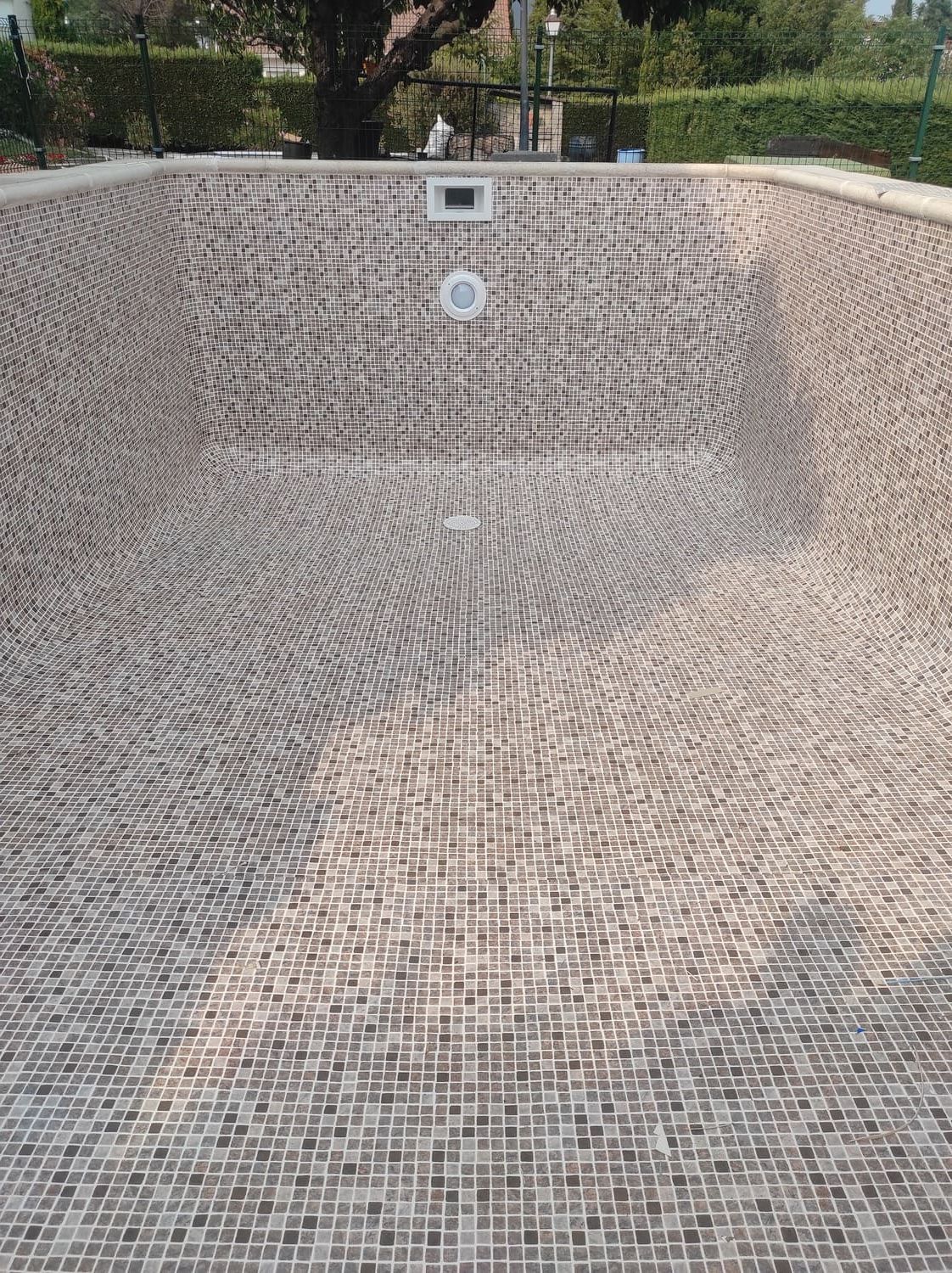Piscina vacía con interior de mosaico; se ve un desagüe rectangular en el extremo profundo.