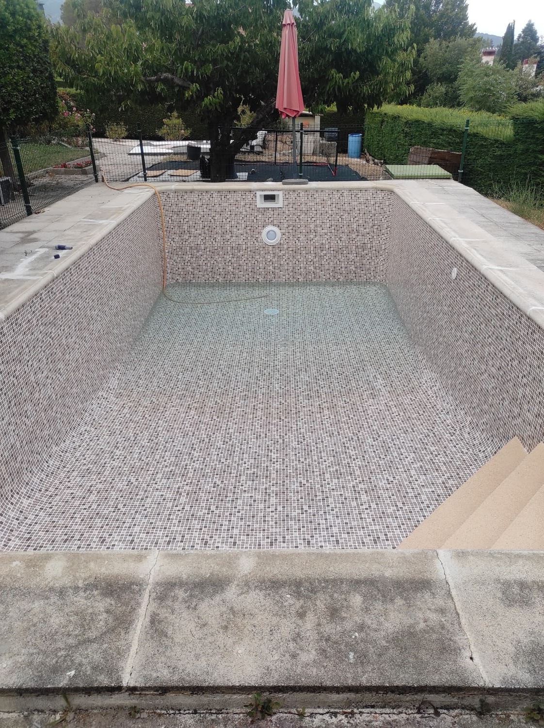 Piscina rectangular vacía con interior de mosaico, rodeada de borde de piedra.