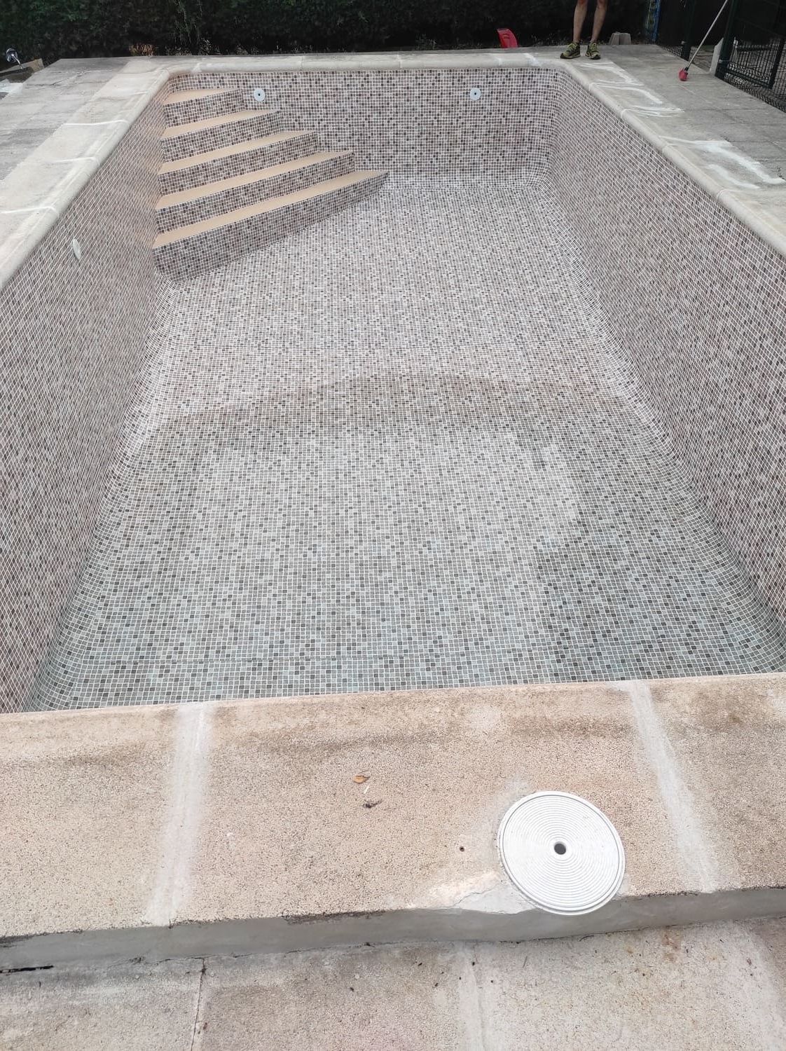 Piscina rectangular vacía con borde de piedra e interior de mosaico.