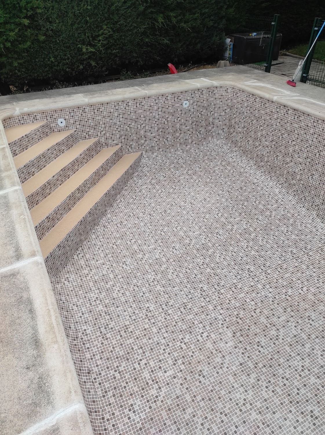 Piscina con baldosas de guijarros, escalones de color beige y borde de piedra.