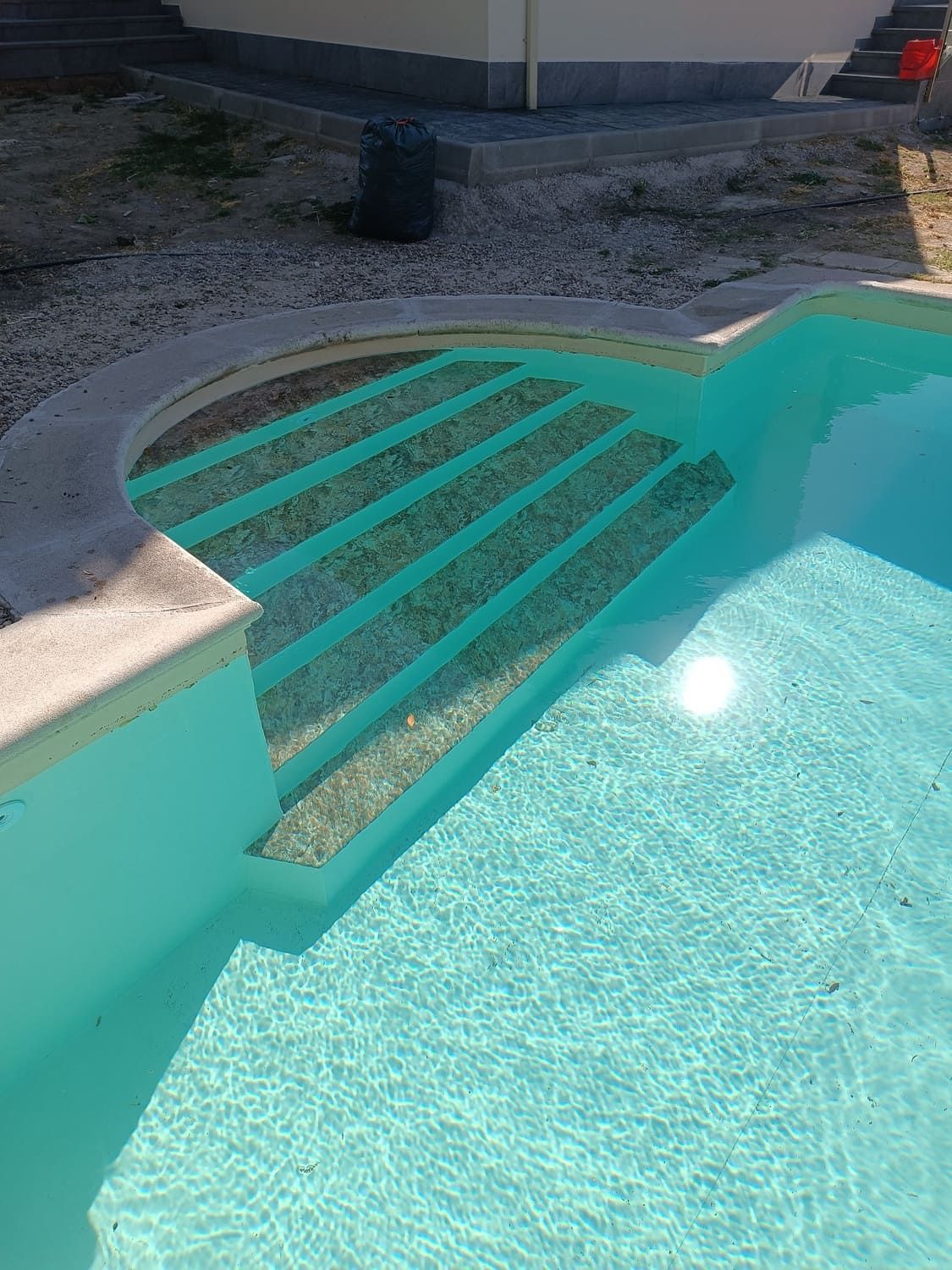 Piscina con agua azul claro y escalones, borde blanco y entorno de grava.