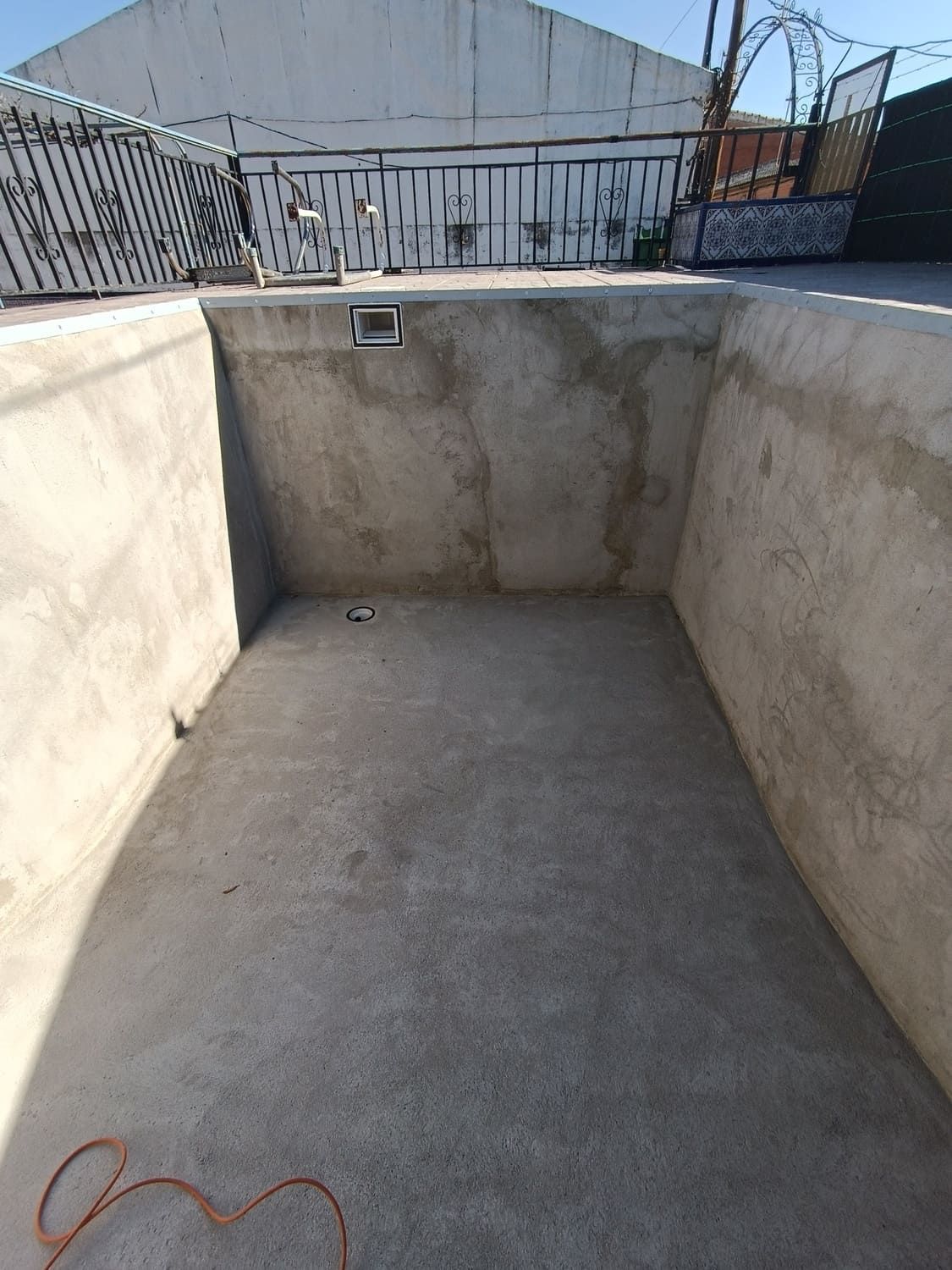 Piscina de hormigón vacía, de forma rectangular, con paredes y suelo de color gris, al aire libre.