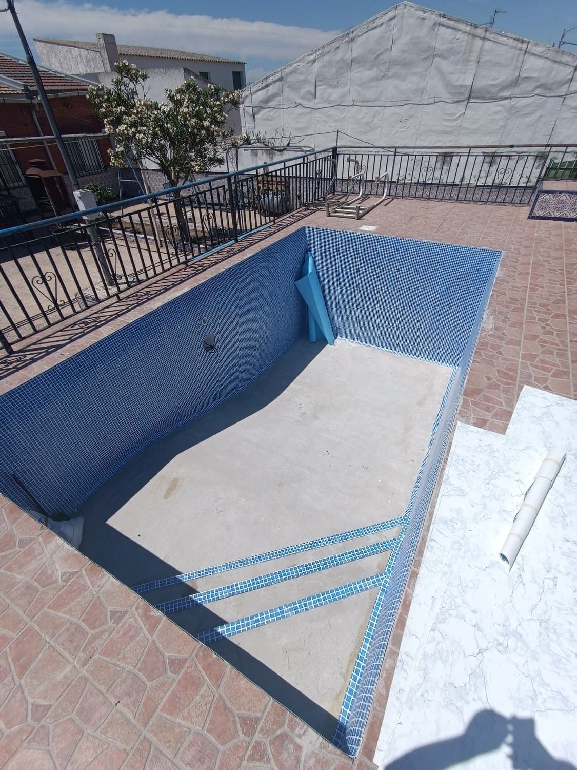 Piscina en construcción; azulejo azul, base de concreto, patio marrón.