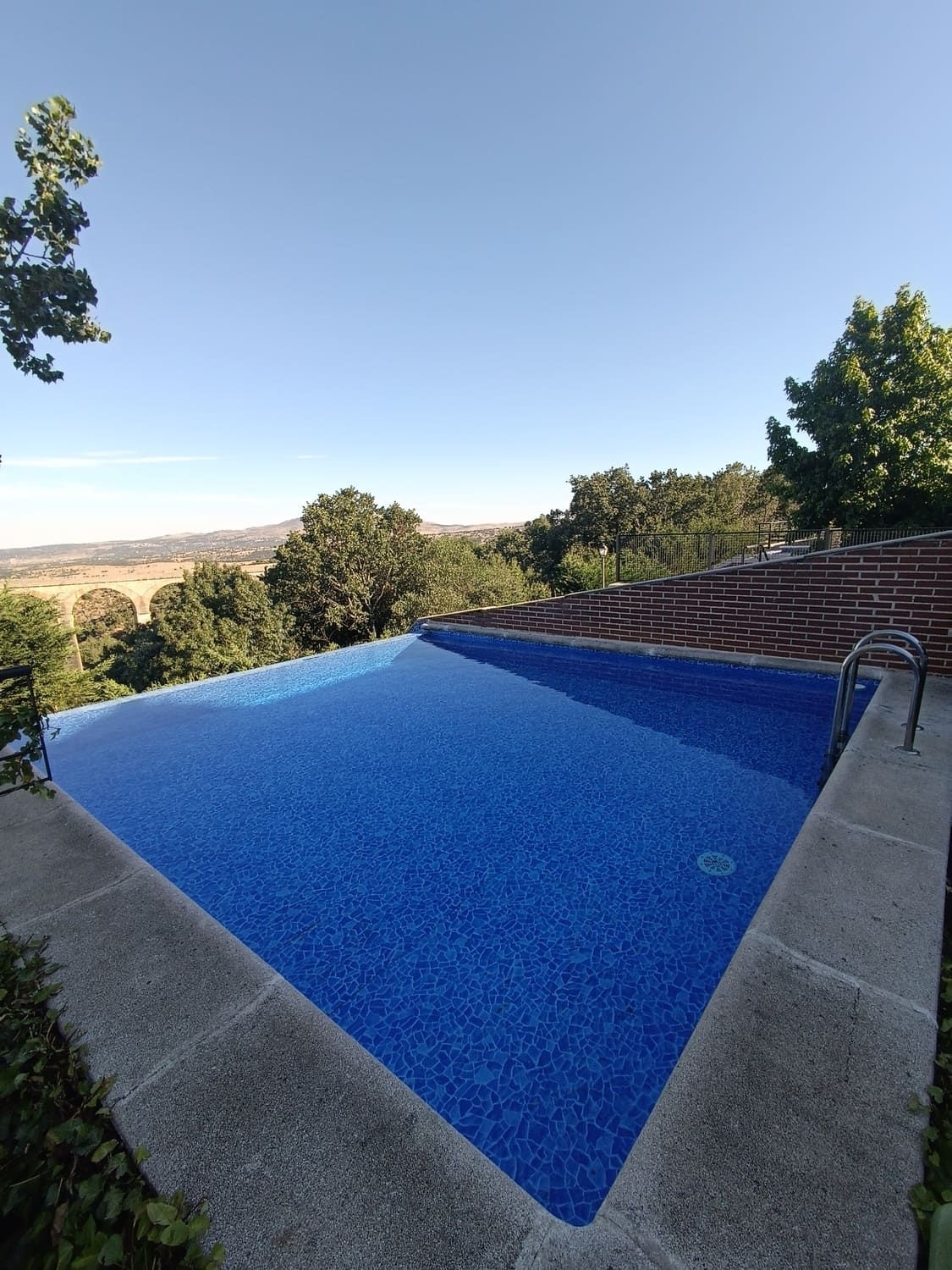 Piscina de azulejos azules al aire libre, con vistas a un paisaje de campos y árboles.