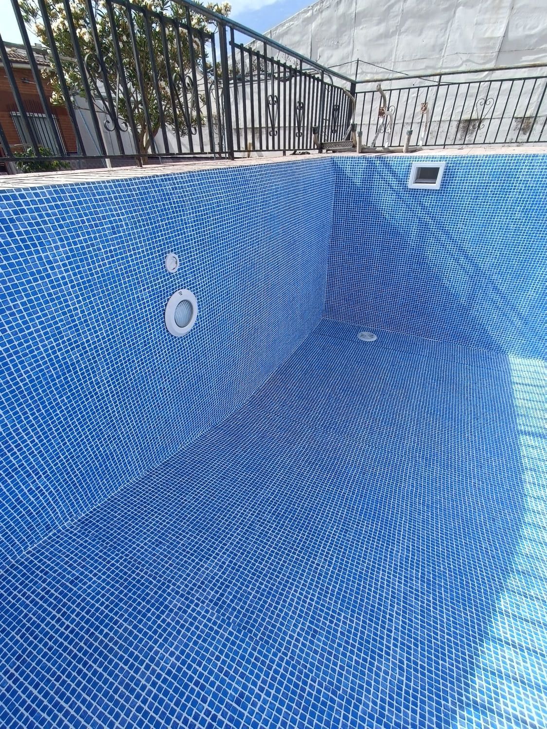 Piscina vacía de azulejos azules con barandillas de metal encima.