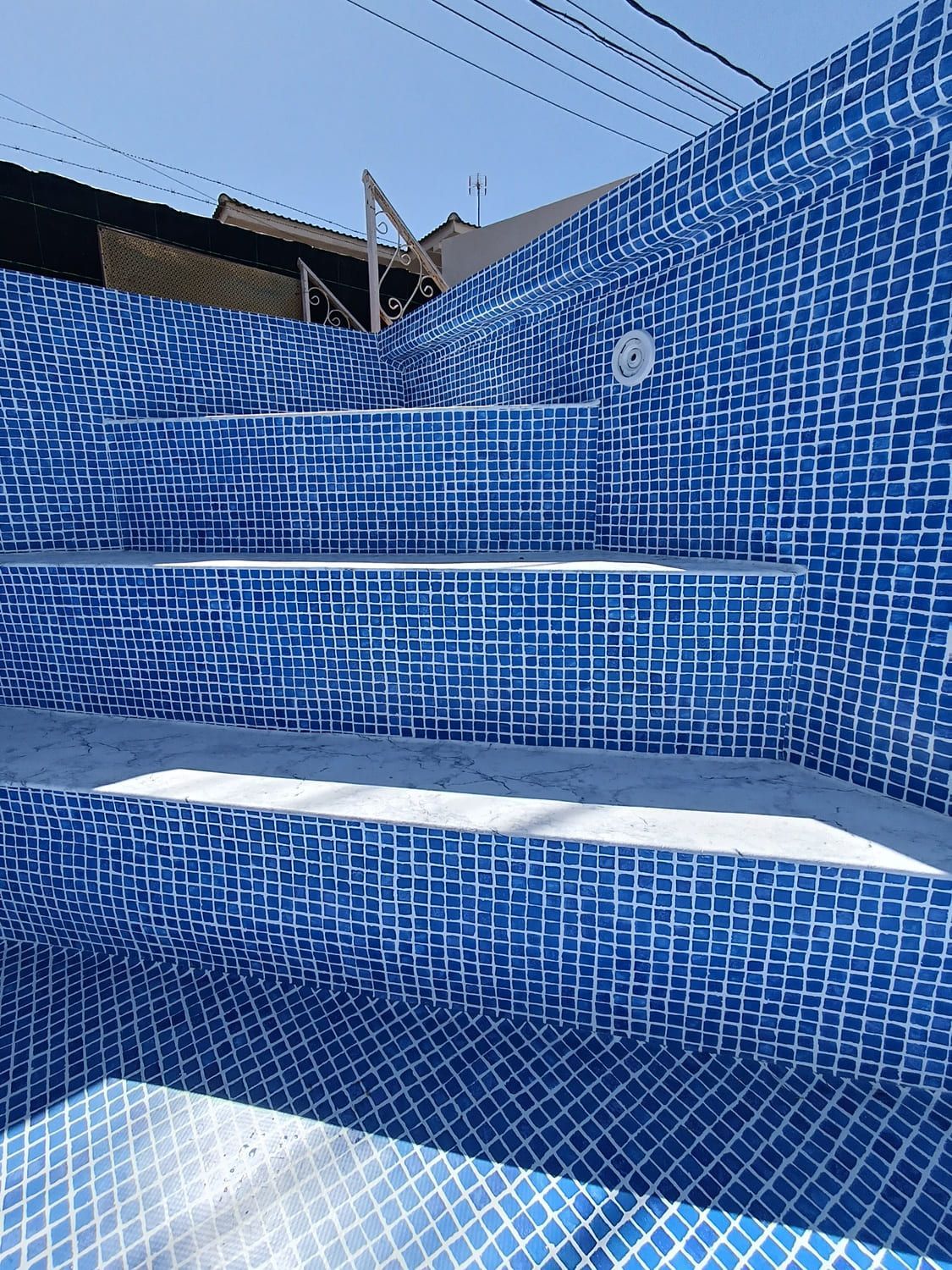 Escaleras de piscina con azulejos azules. Azulejos de mosaico azul y blanco brillante cubren las paredes y escaleras de una piscina vacía.