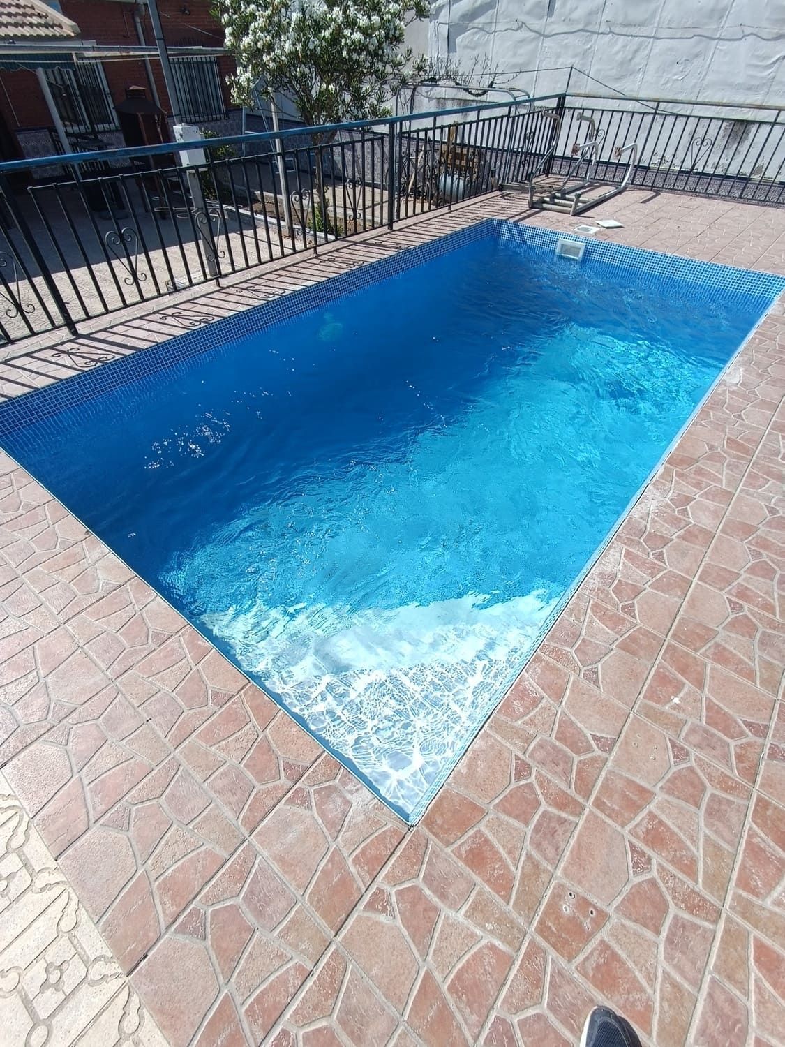 Piscina rectangular de azulejos azules con marco de ladrillo, junto a una valla negra.