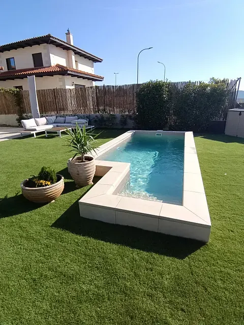 Una piscina en un patio trasero con una casa al fondo.