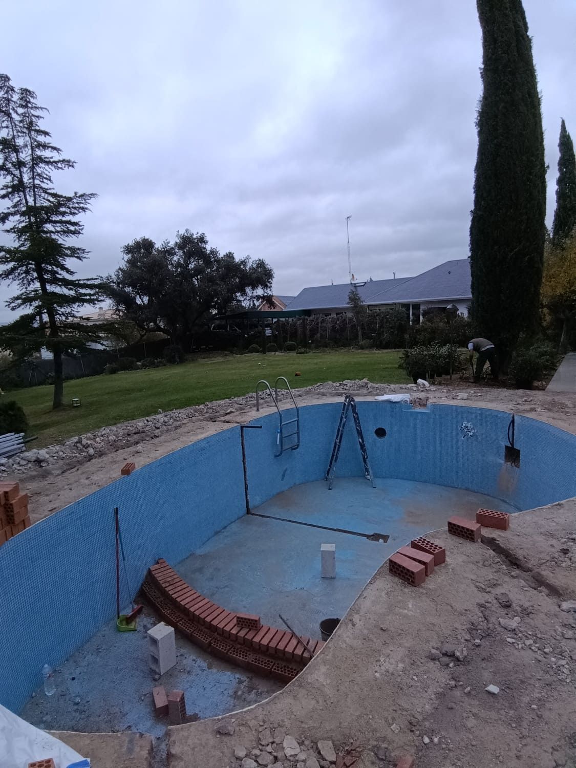 Piscina en construcción con azulejos azules y ladrillos circundantes en un día nublado.
