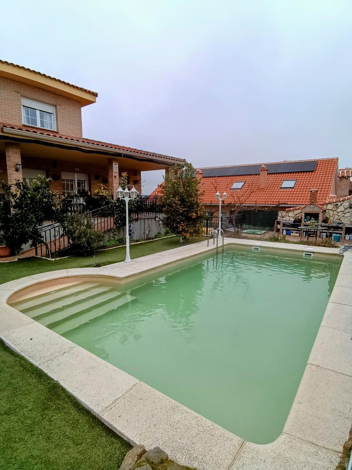 Piscina junto a una casa con fachada de ladrillo y cielo nublado.