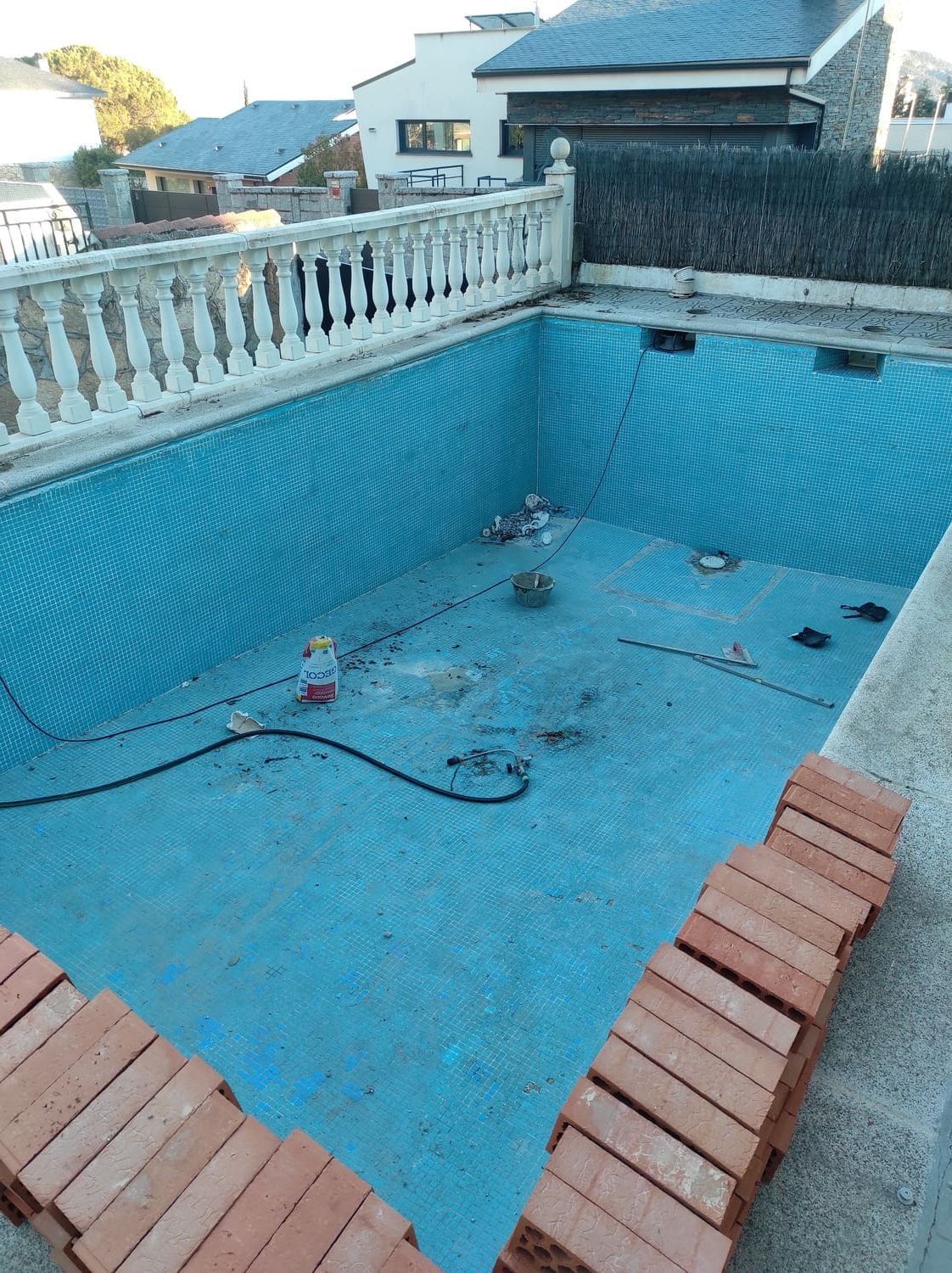Piscina vacía en proceso de renovación, con interior de azulejos azules y ladrillos apilados.