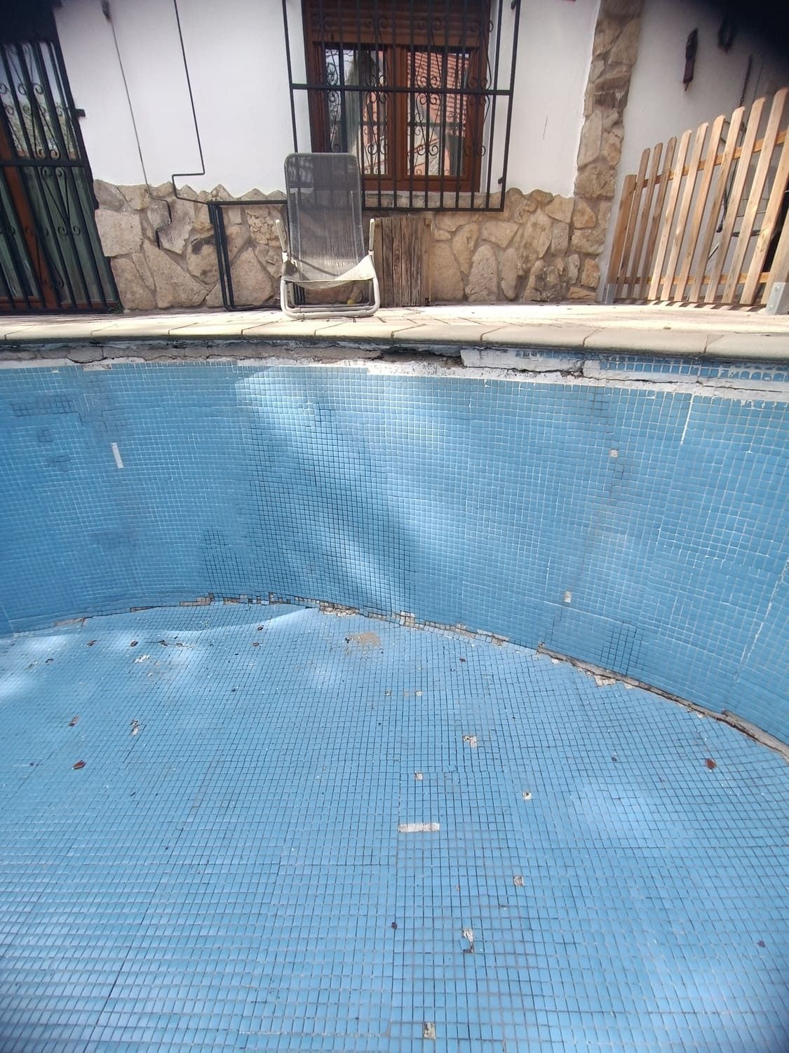 Piscina vacía de azulejos azules. Al fondo, una tumbona junto a una ventana.