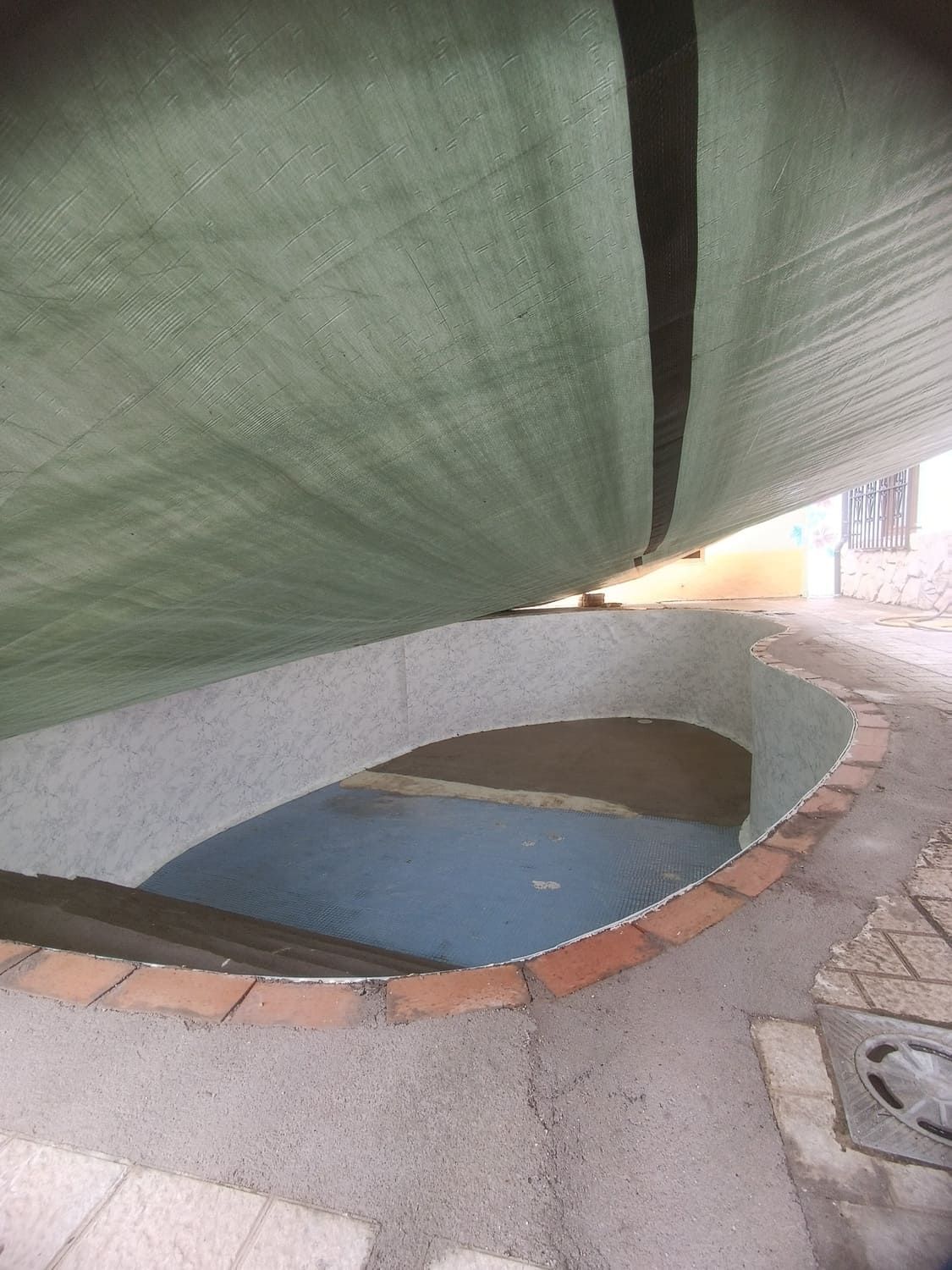 Una lona verde cubre una estructura curva, de paredes bajas y con molduras de ladrillo, lo que da lugar a una superficie azul.